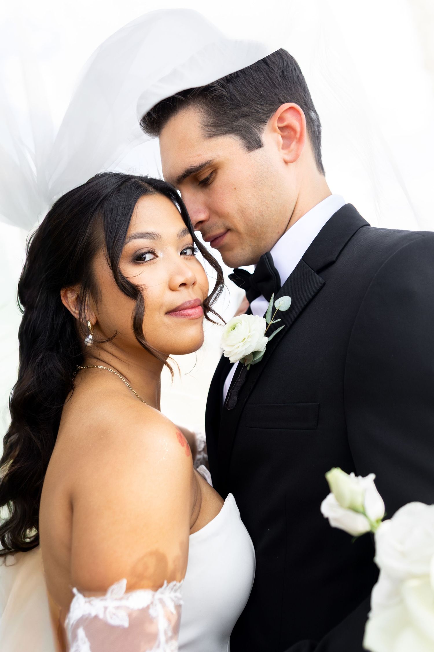 Romantic wedding portrait of newlyweds in classic black and white attire with white floral accents.