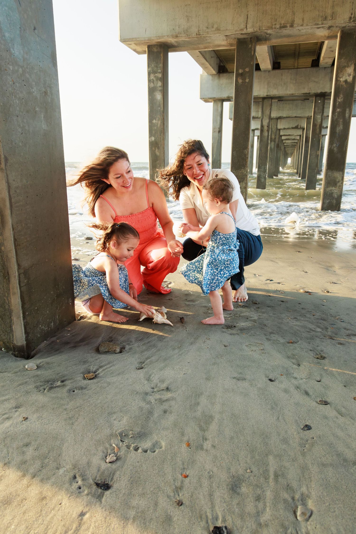 A sequence of people crouching down to examine something in the sand under a beach pier.