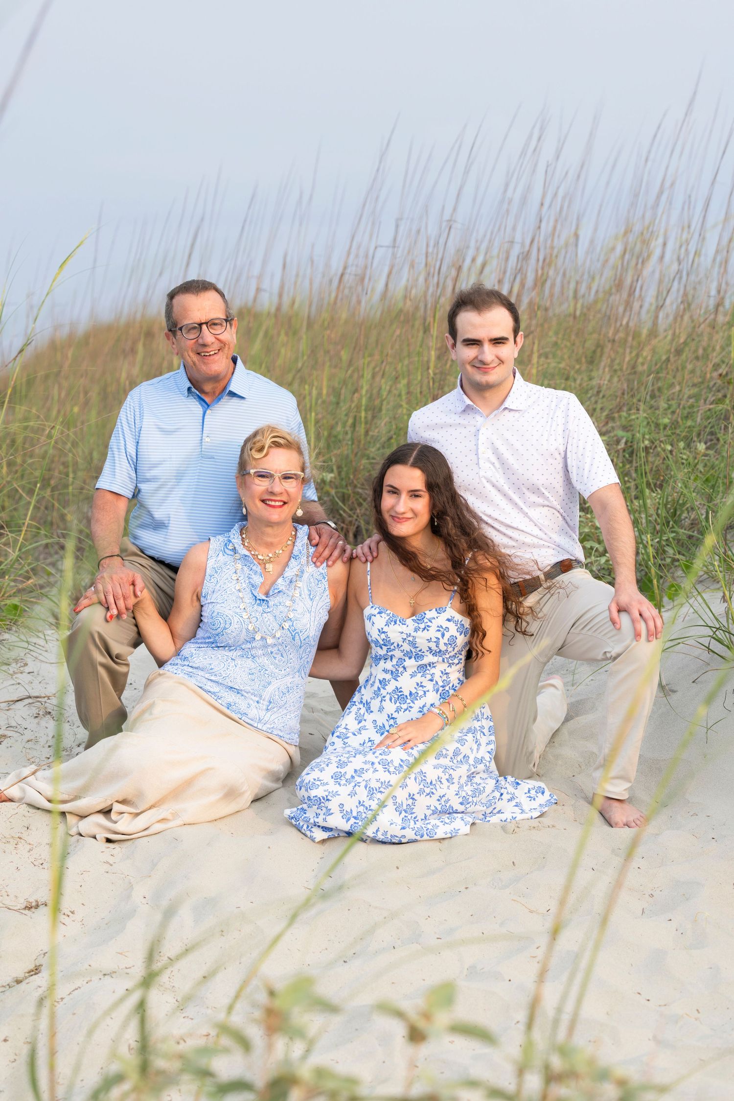 A group poses together on a sandy beach dune with sea grass in the background on a cloudy day.
