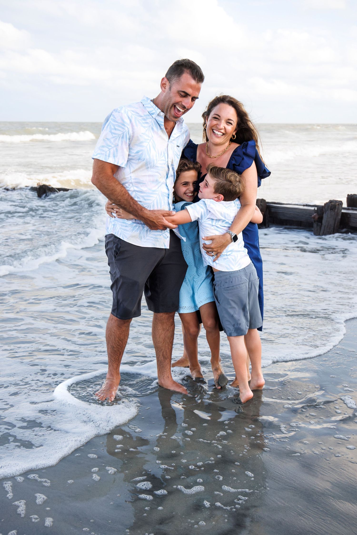 Happy family enjoying time together at the beach while standing in shallow ocean waves at sunset.