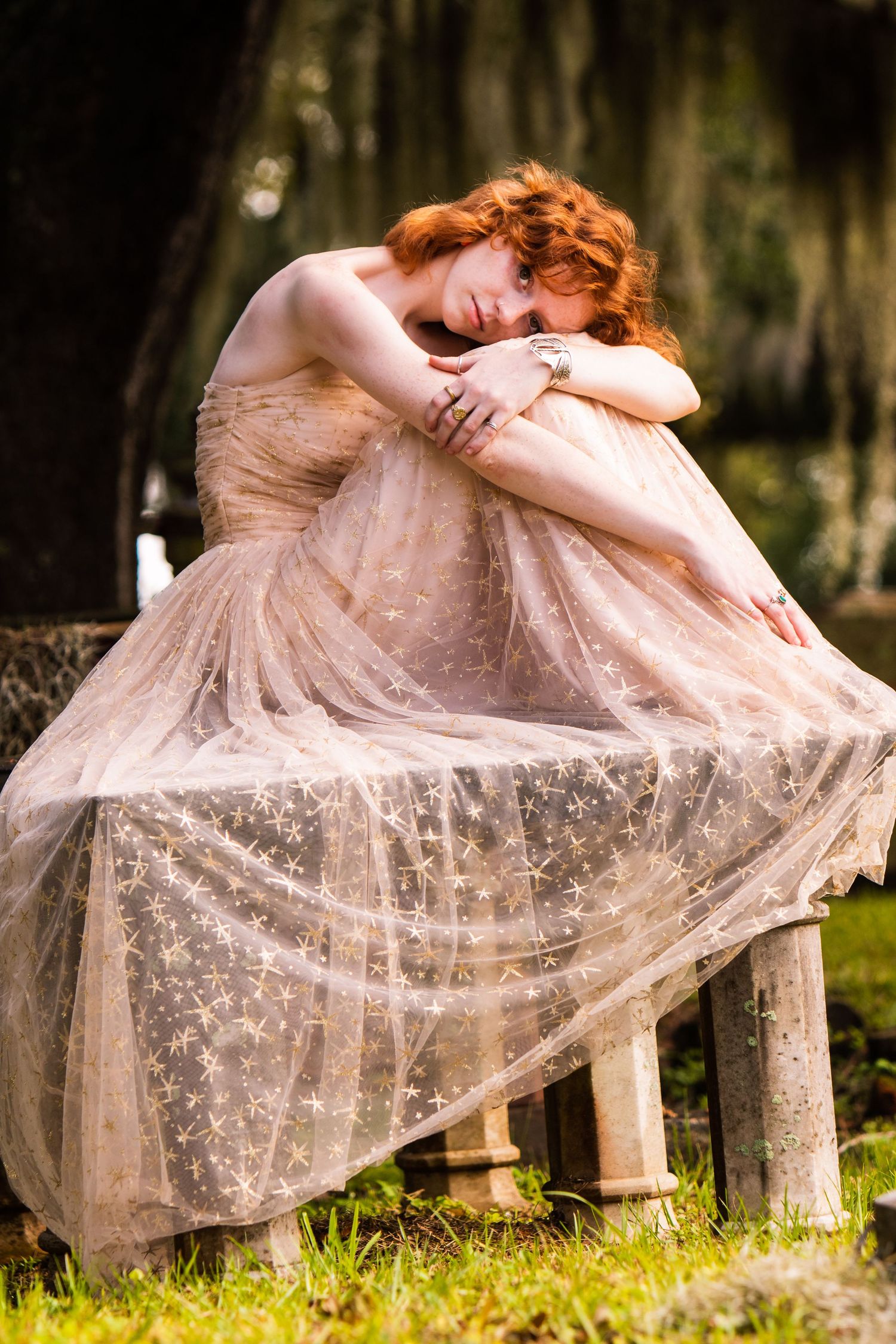 A person in a flowing blush tulle gown rests on a stone bench in a dreamy outdoor garden setting.
Charleston Portrait Session