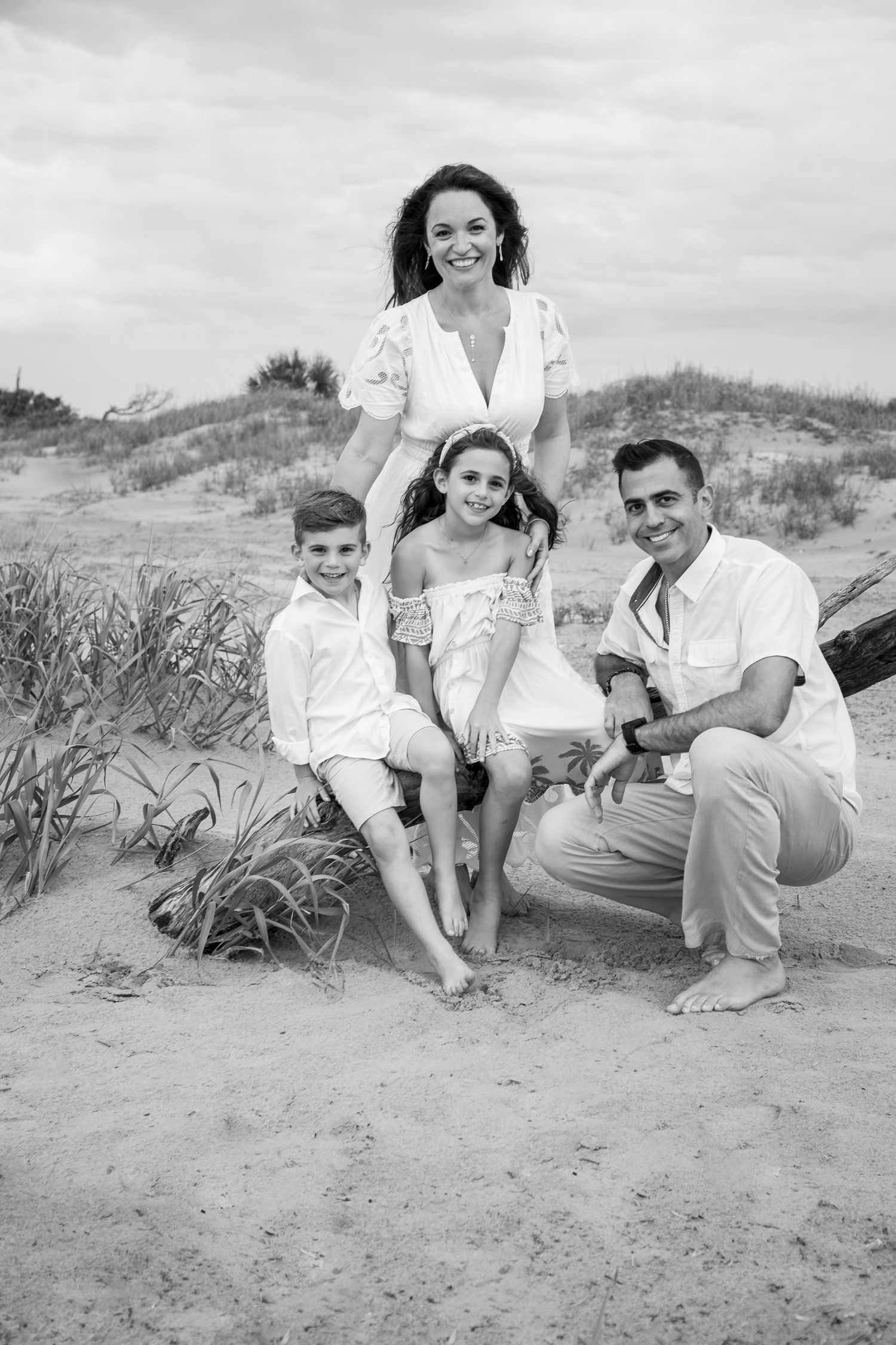 A family in white clothing poses together on a sandy beach dune in this vintage black and white photograph.