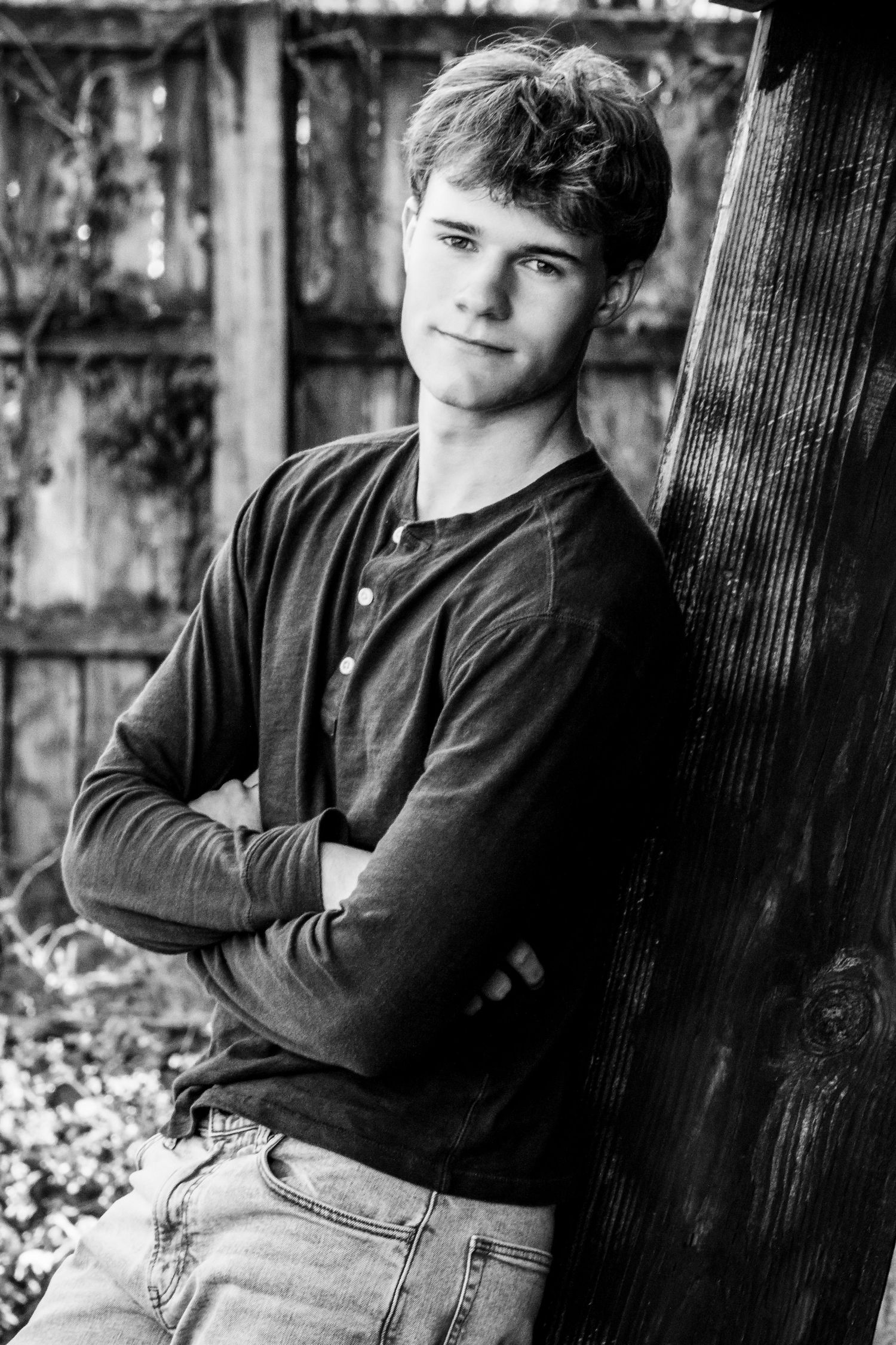 Black and white portrait series showing someone in casual attire leaning against a wooden post in an outdoor setting.