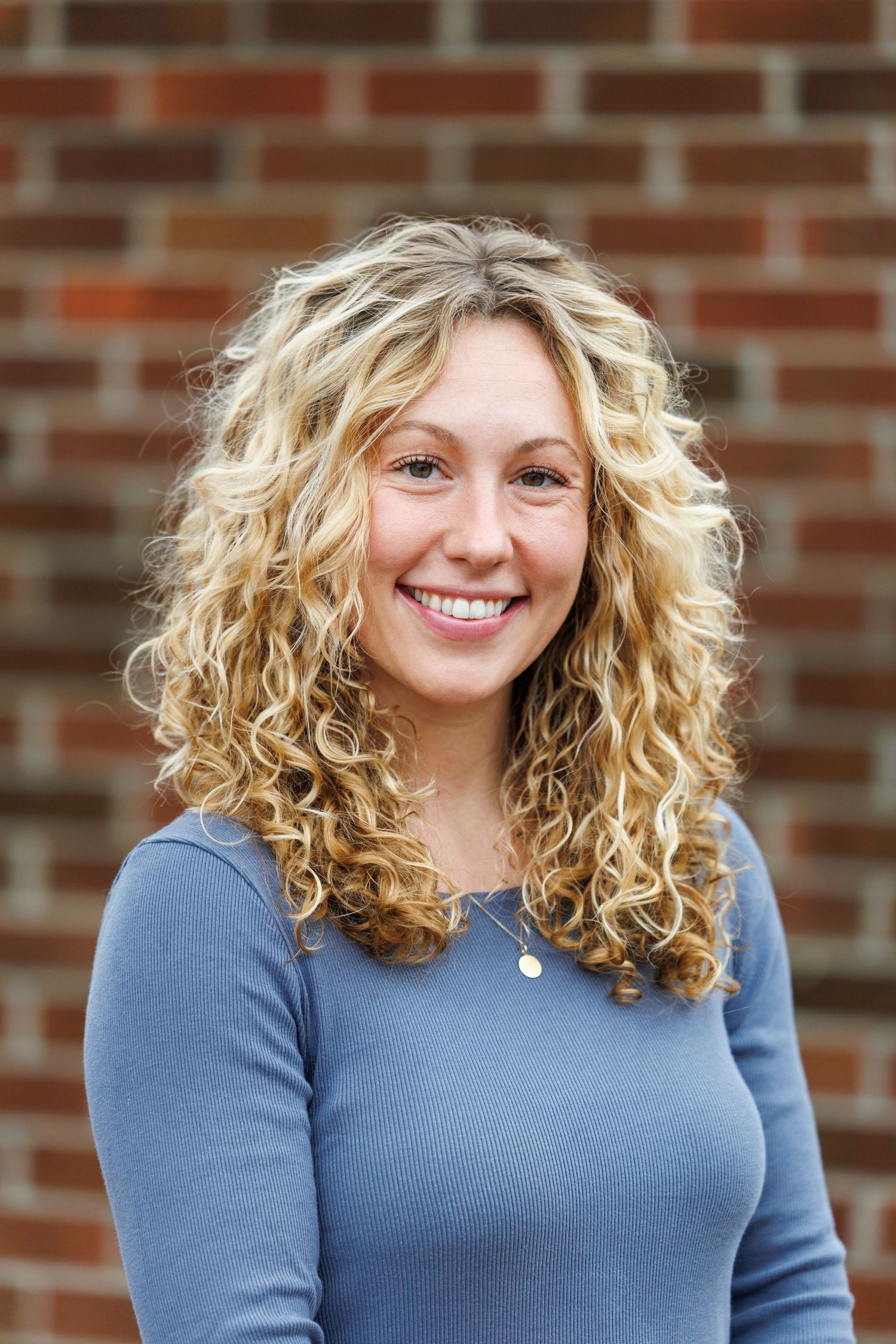 A series of photos showing someone with curly blonde hair wearing a blue sweater against a brick wall background.