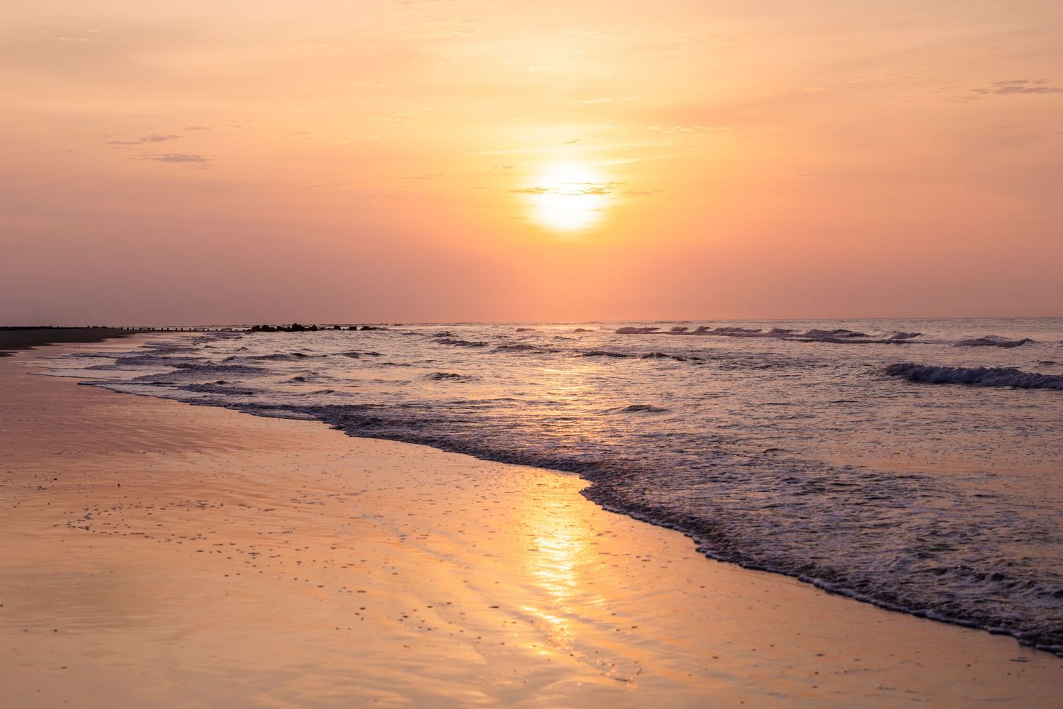 Stunning orange sunset over the ocean horizon creates a golden reflection on the rippling water surface.