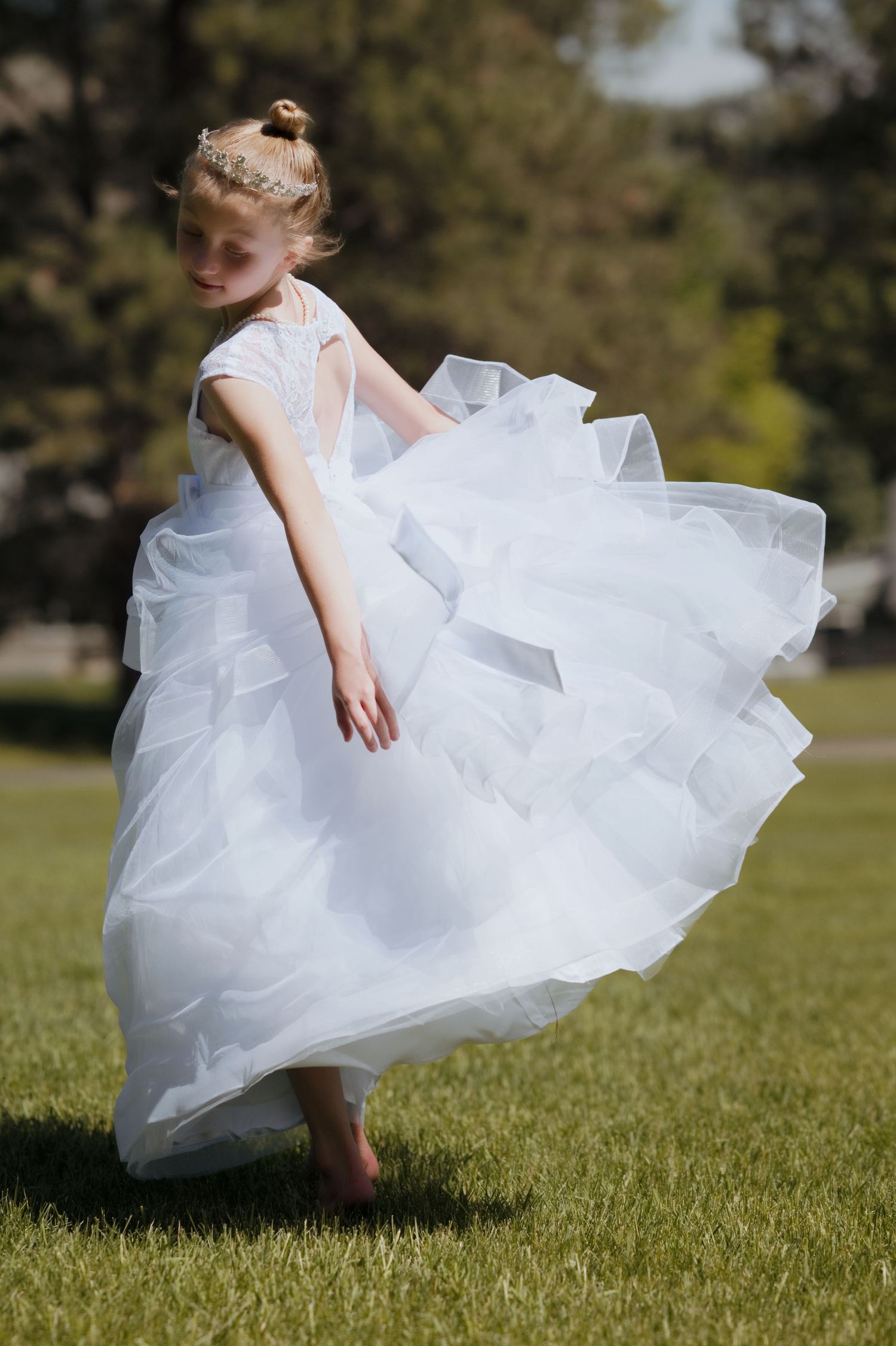 Young girl twirling in a white tulle flower girl dress on green grass outdoors.