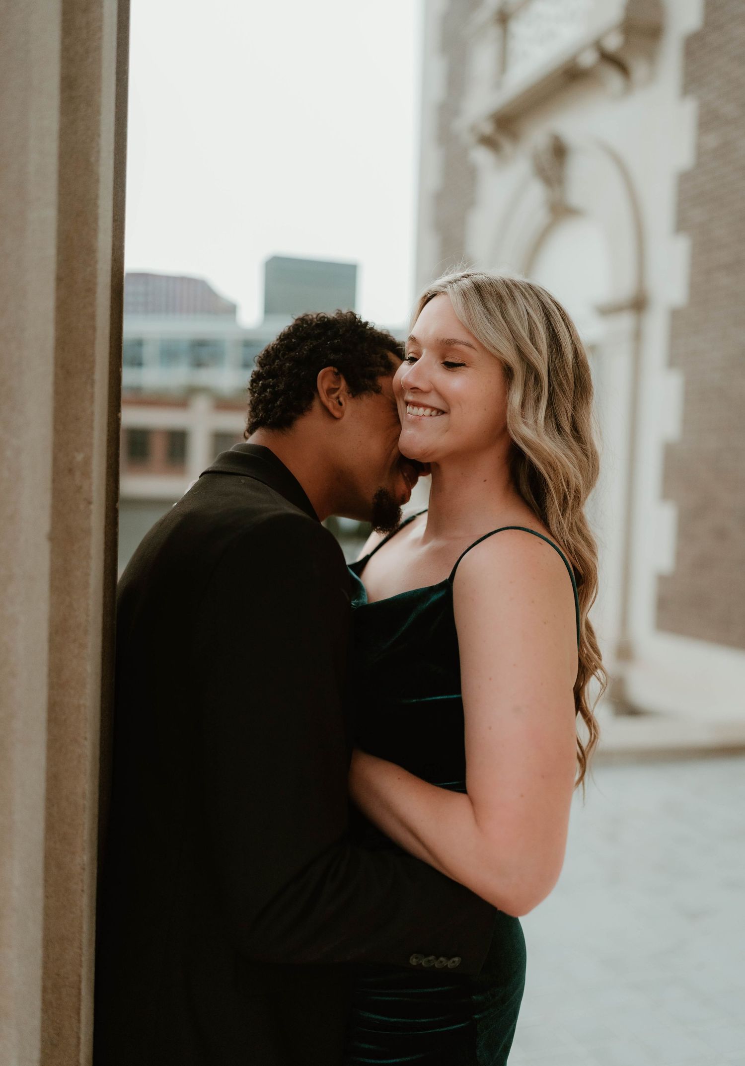A romantic couple embraces in an intimate moment against a building exterior during golden hour.