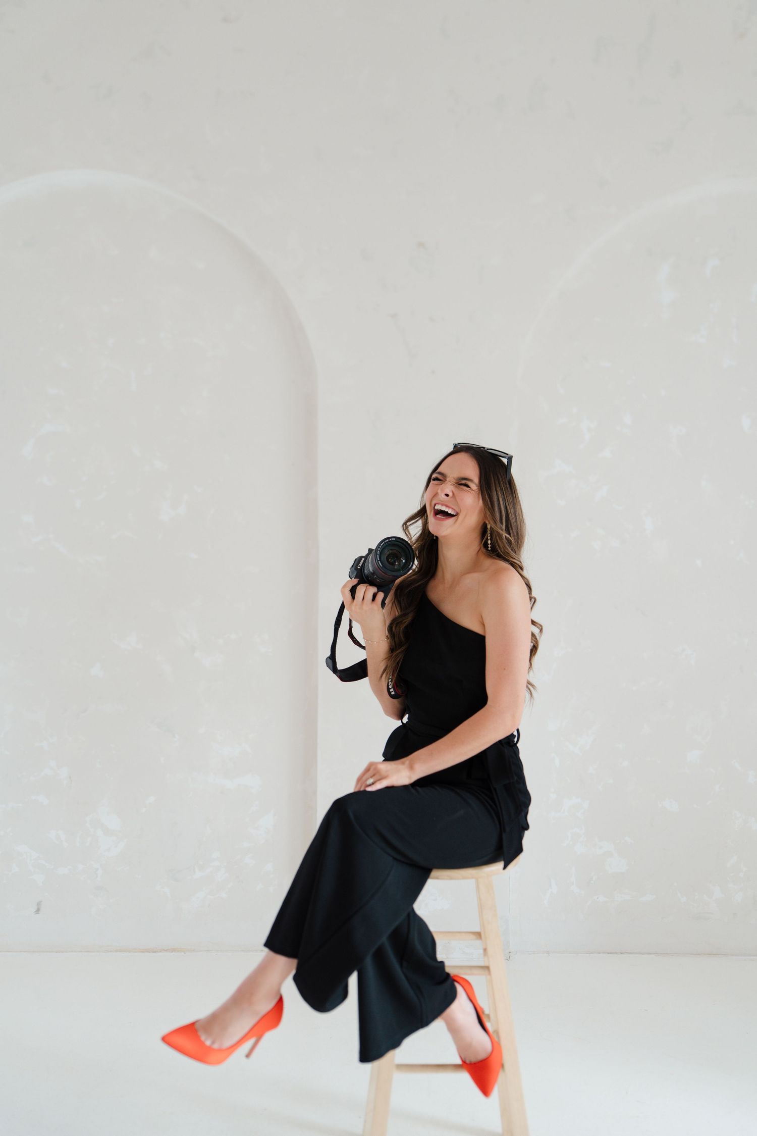 A sequence of joyful photos showing a woman in a black outfit and orange shoes sitting and laughing in a white studio setting.