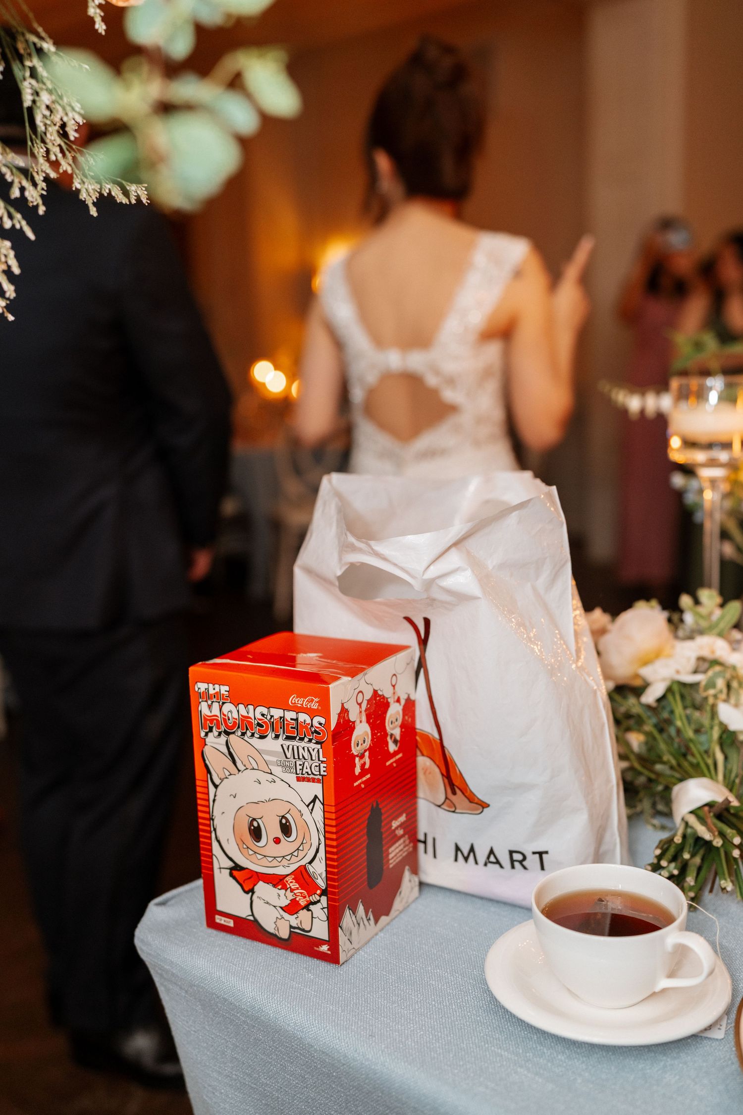 H Mart shopping bag and cartoon panda snack box sit next to a tea cup at an elegant wedding reception table.
