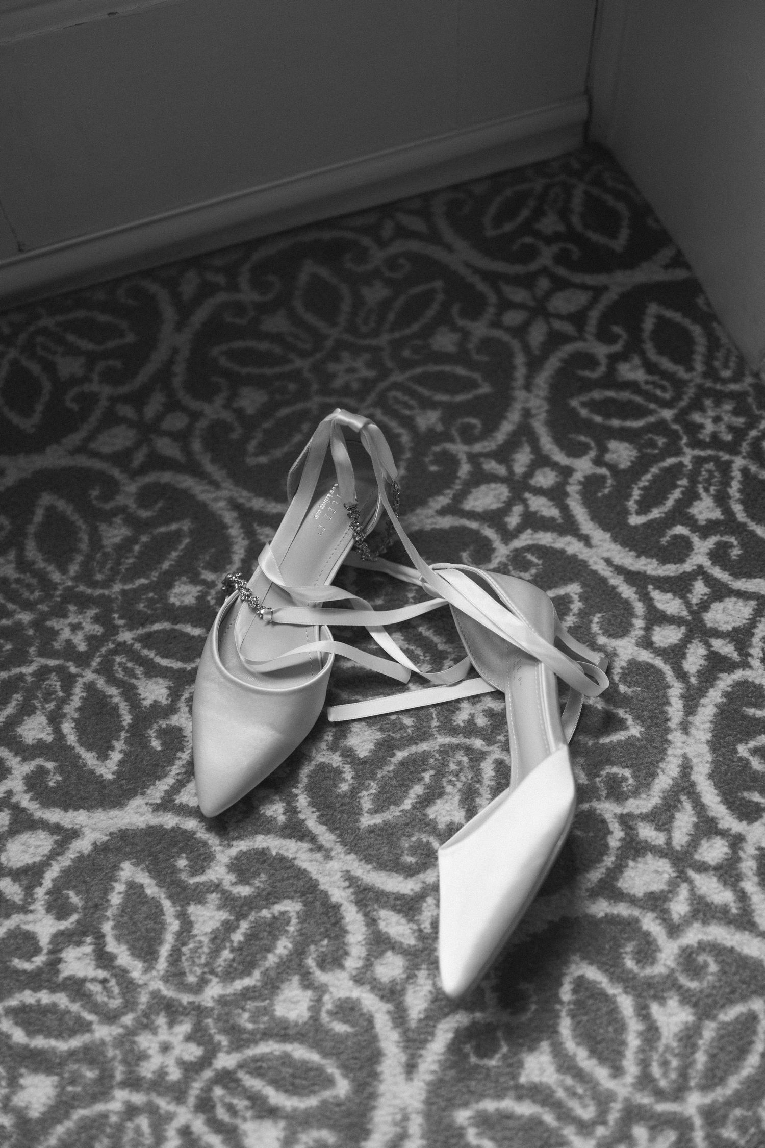 A pair of elegant white ankle-strap high heel shoes placed on a decorative patterned carpet in black and white.