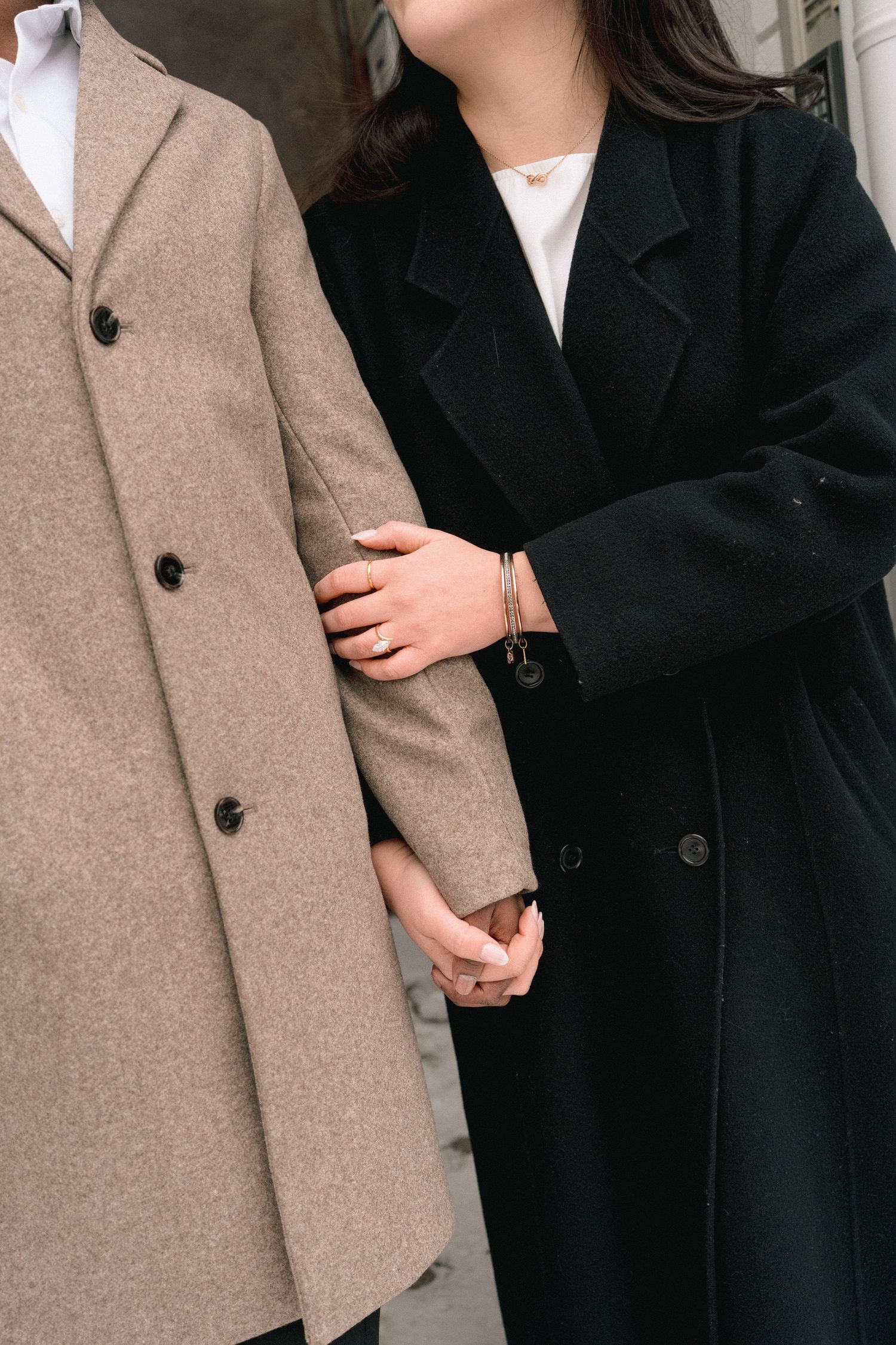 Close-up of two people wearing contrasting beige and black wool coats holding hands together.