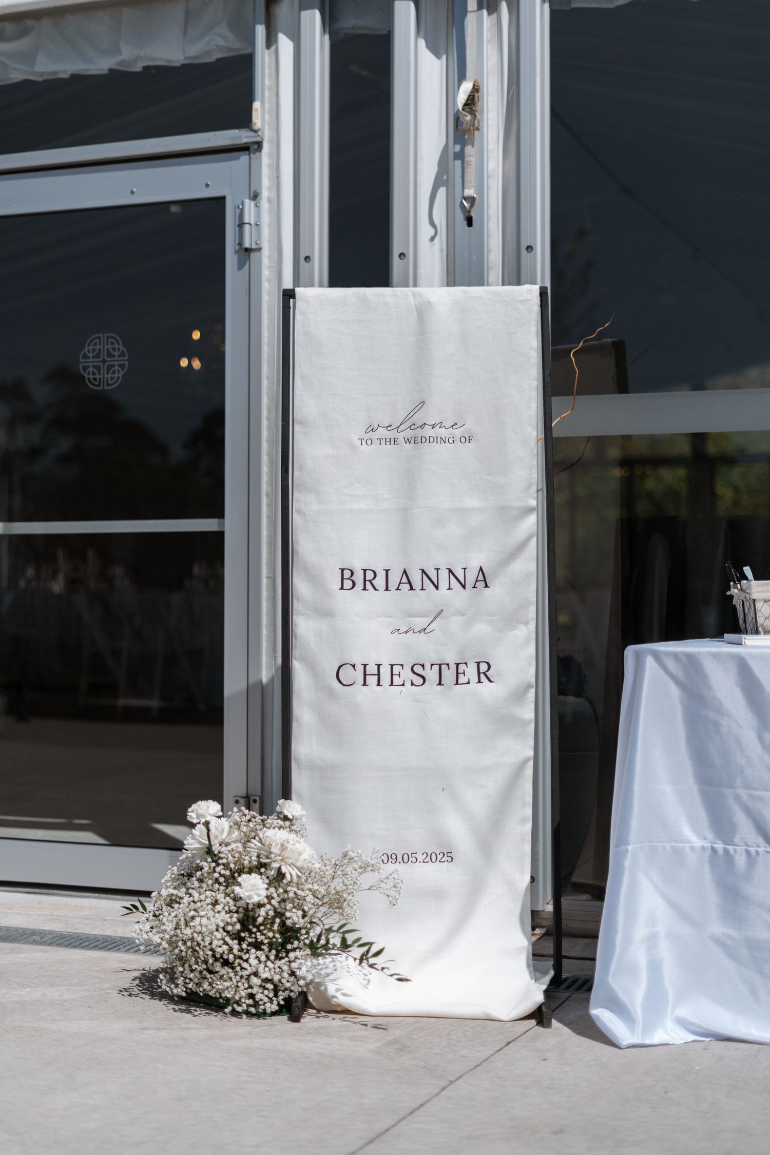 An elegant white wedding banner with names displayed features baby's breath flowers at its base.