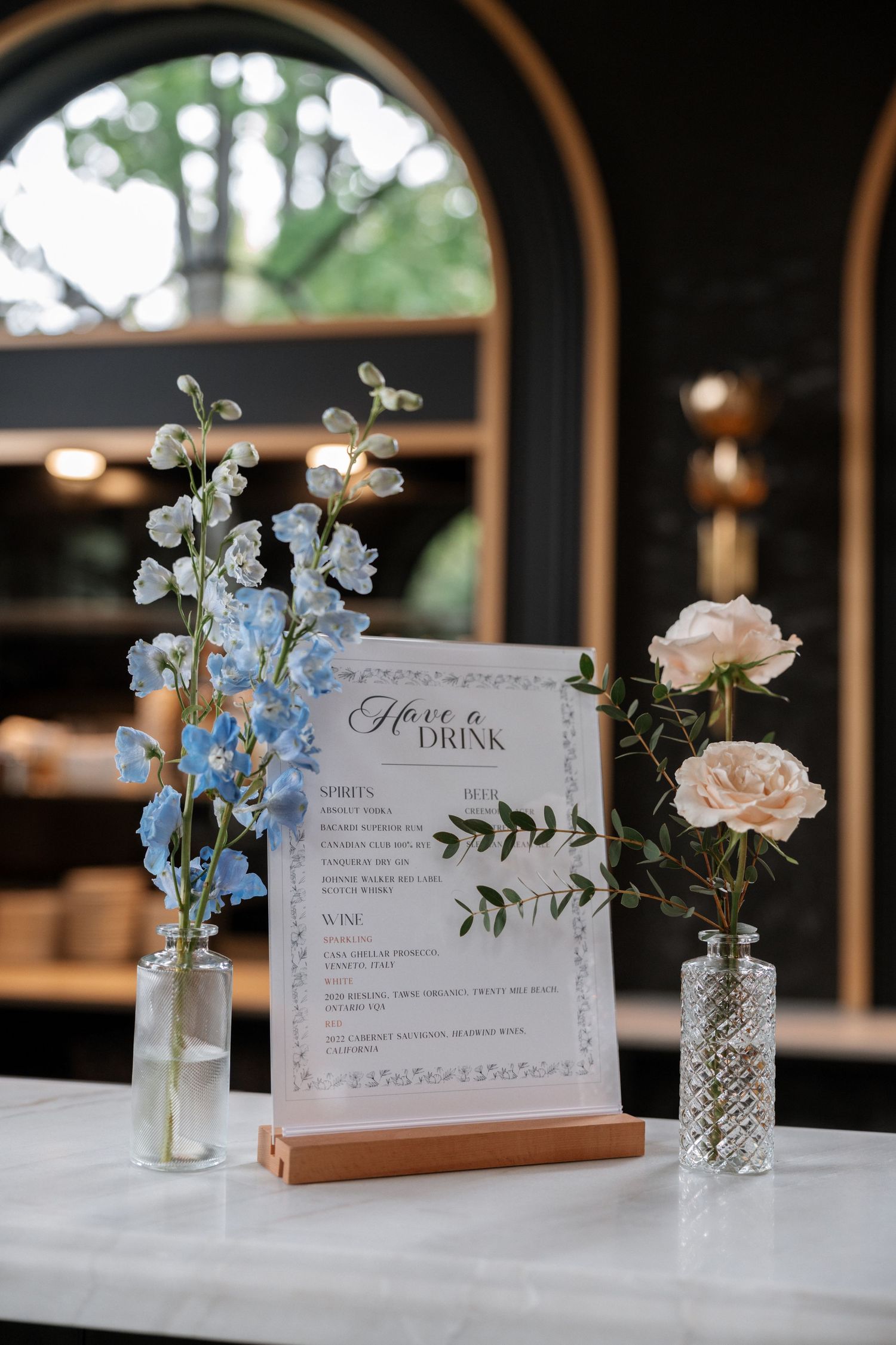 Wedding menu display with delicate floral arrangements in glass vases on white tablecloth.