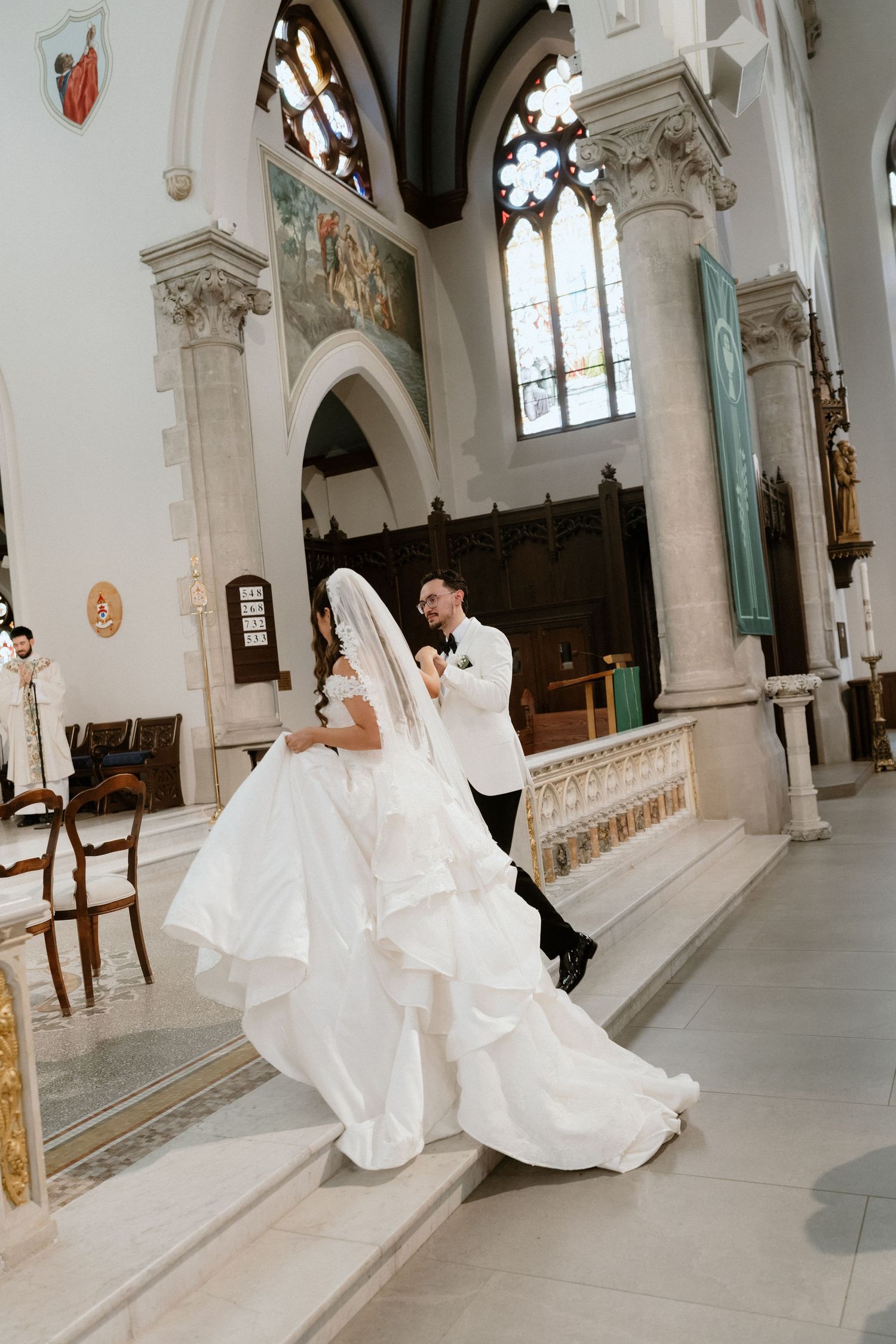 Bride and groom dancing in a grand church aisle, bride in a flowing white gown with veil, groom in black tuxedo.