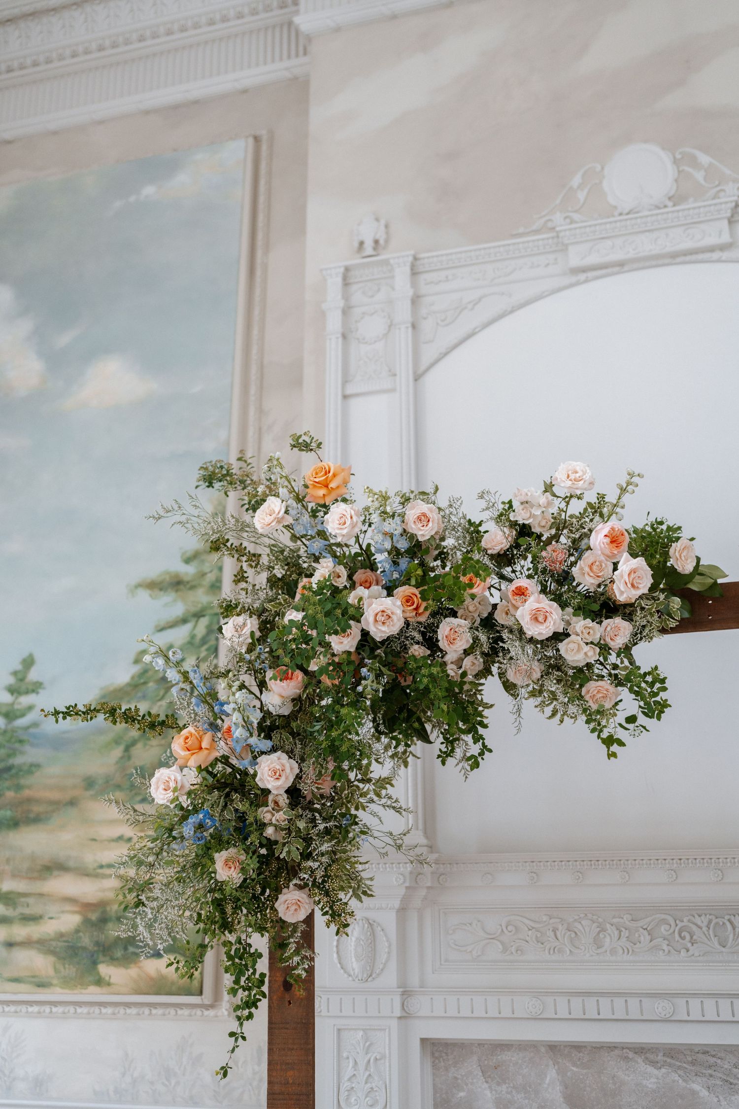 Lush floral arrangement of peach and blue roses cascading over a white fireplace mantel.