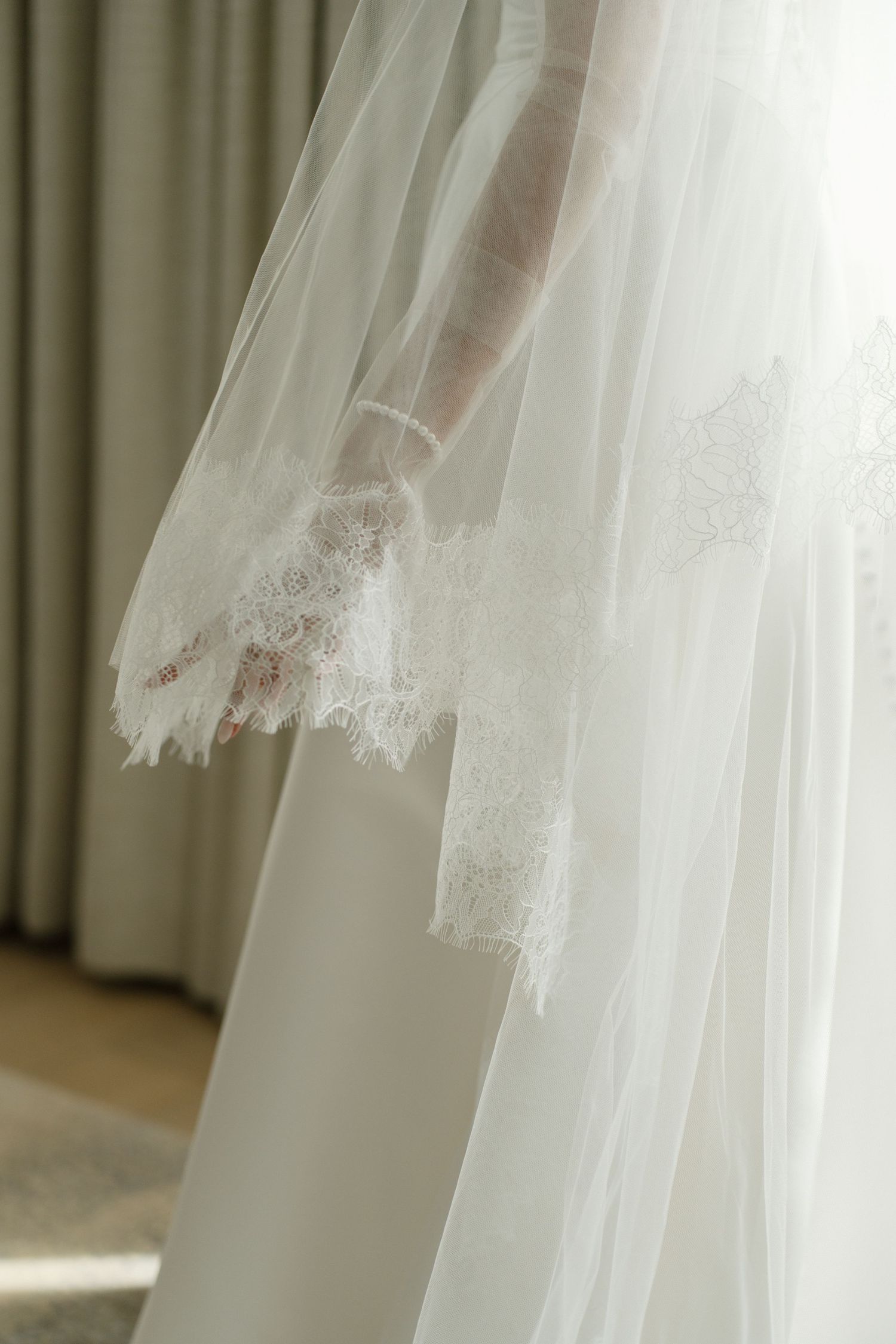 Close-up of a bridal veil with delicate lace trim detail, soft white tulle fabric flowing elegantly in natural light.