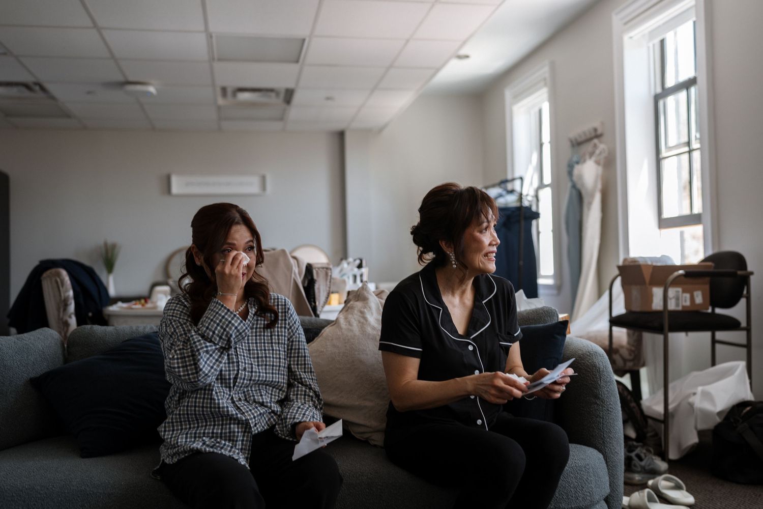 Two people sitting on a dark couch in an office space, working on mobile devices in natural lighting.