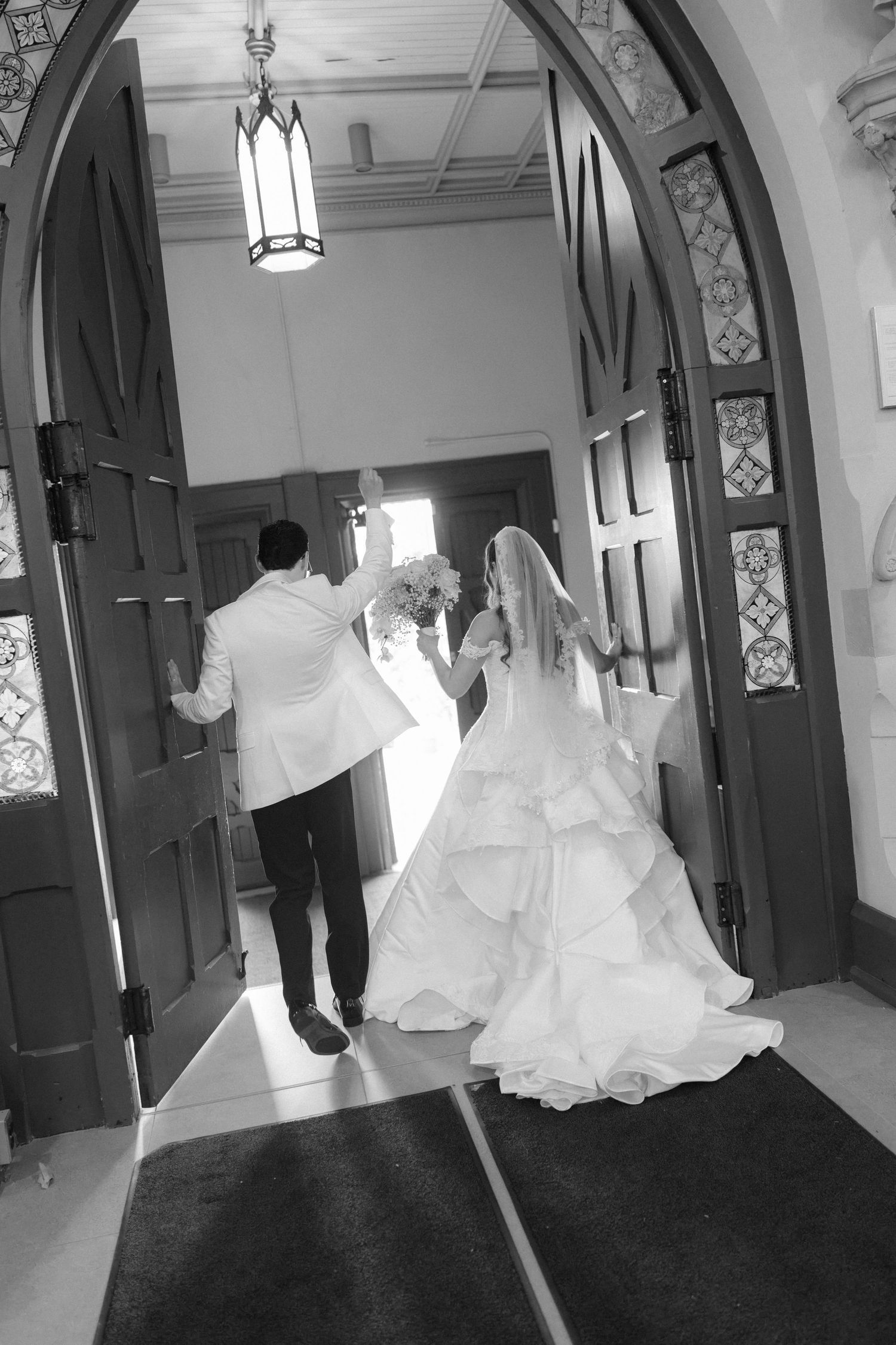 Black and white photo of bride and groom walking through church doors on wedding day.