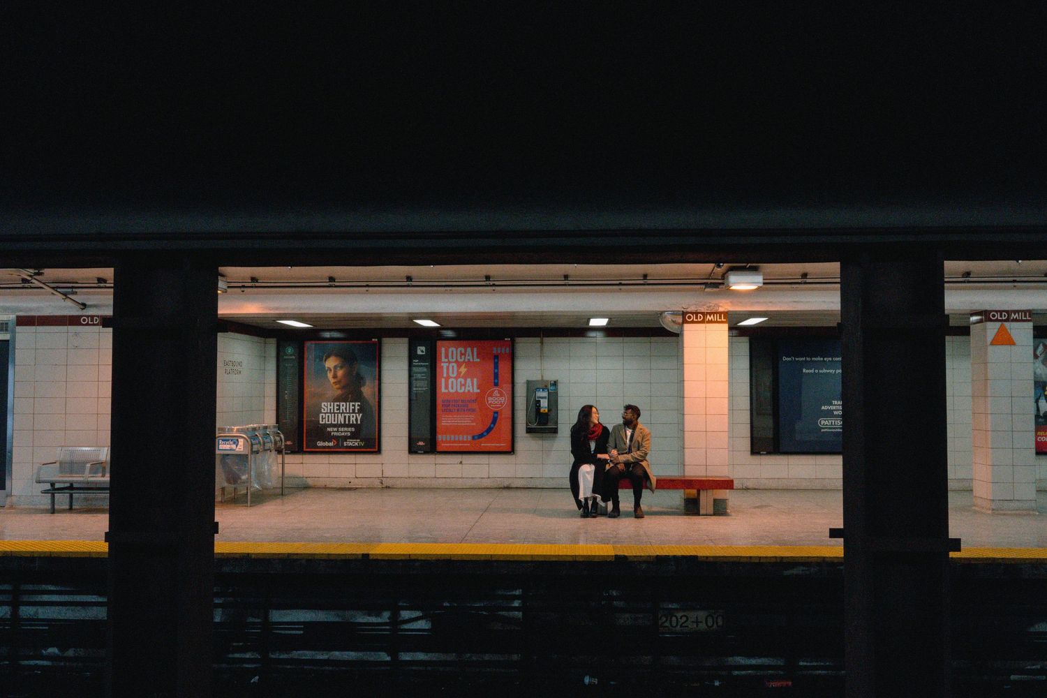 A dark subway station platform with fluorescent lighting and pillars casting shadows in the distance.