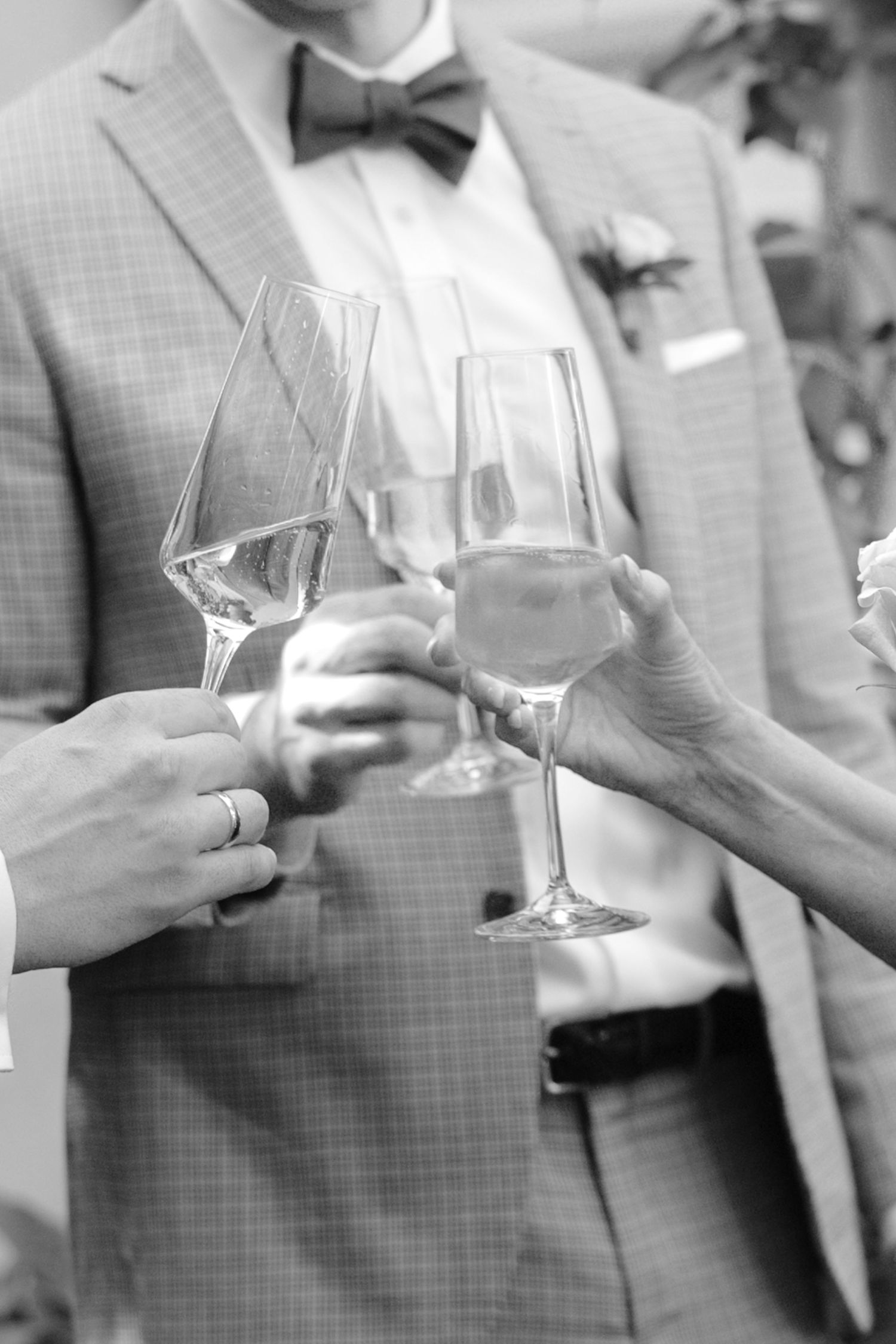 Black and white photo of people toasting with champagne glasses at a wedding celebration.
