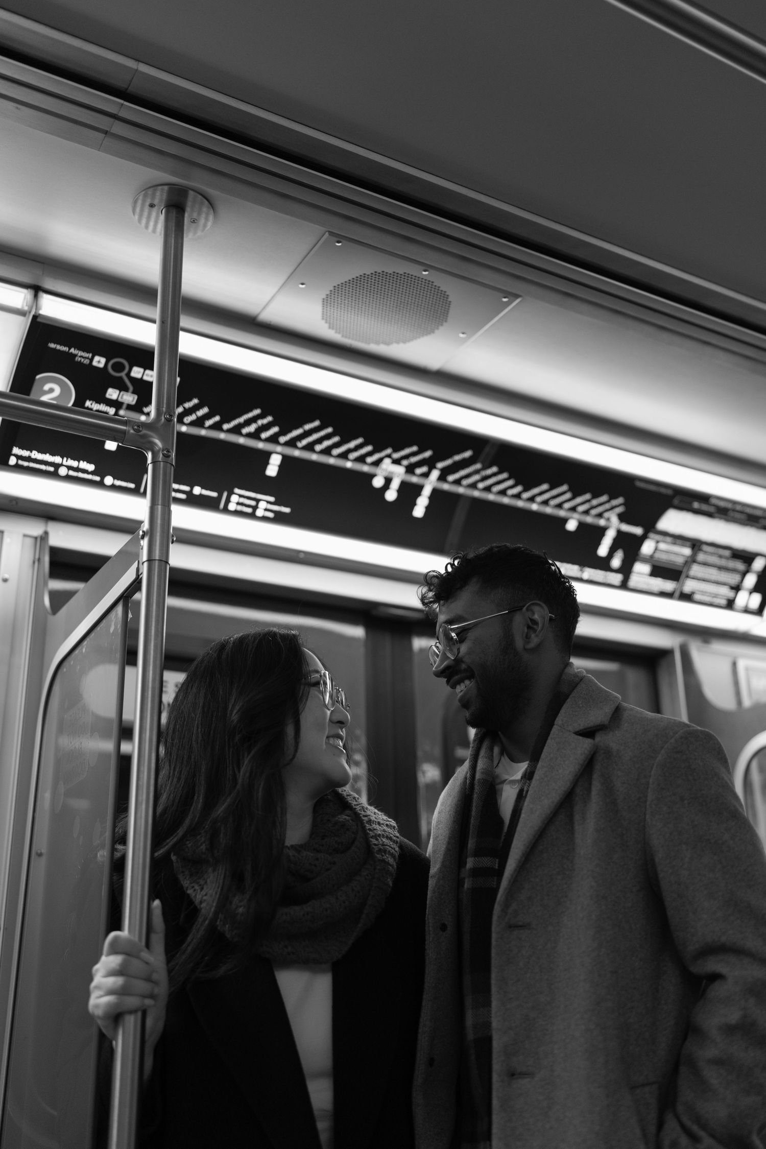 Passengers laugh and smile together while riding in a black and white subway car interior.