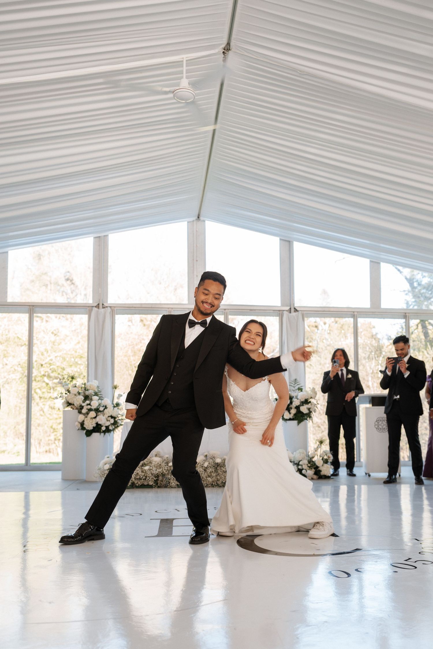 A joyful couple dances together in an elegant white chapel venue decorated with floral arrangements during their wedding celebration.