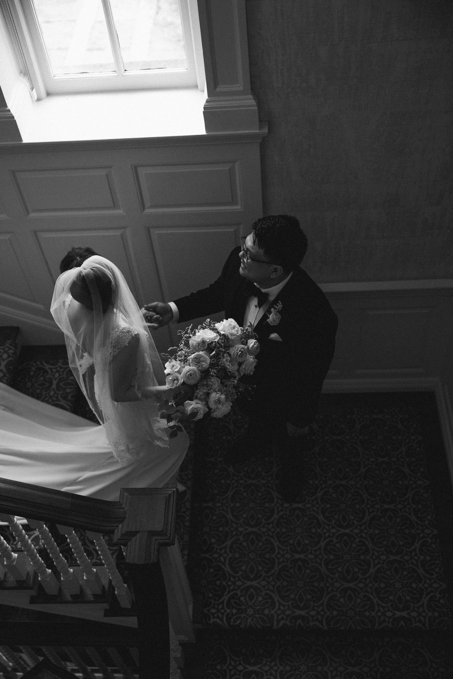 A dramatic black and white wedding photo shows a couple on a staircase with the bride holding an elegant floral bouquet.