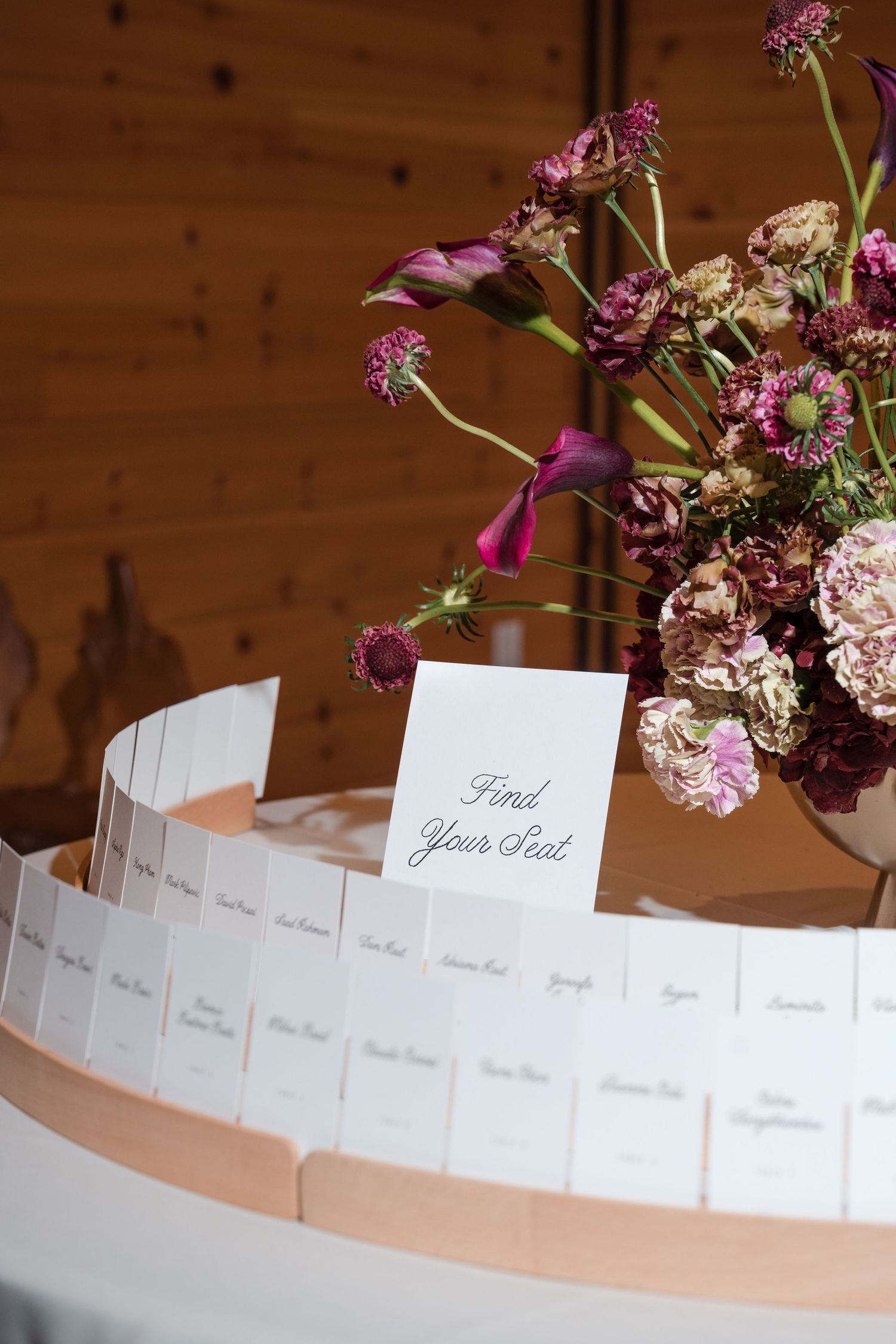 Wedding seating chart display with white escort cards and purple floral arrangement on a round table.