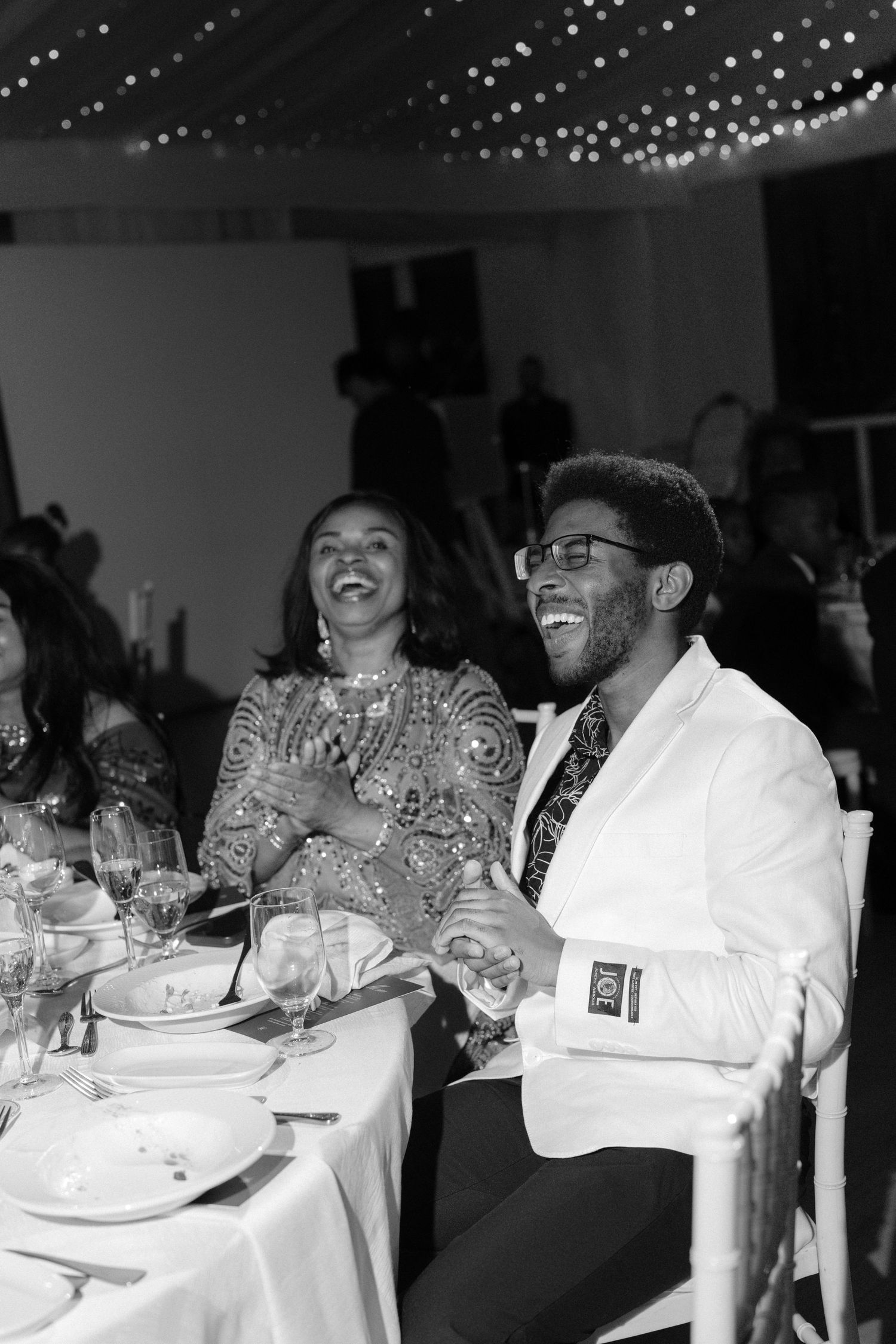 Black and white photo of two people laughing joyfully at a formal dinner event.