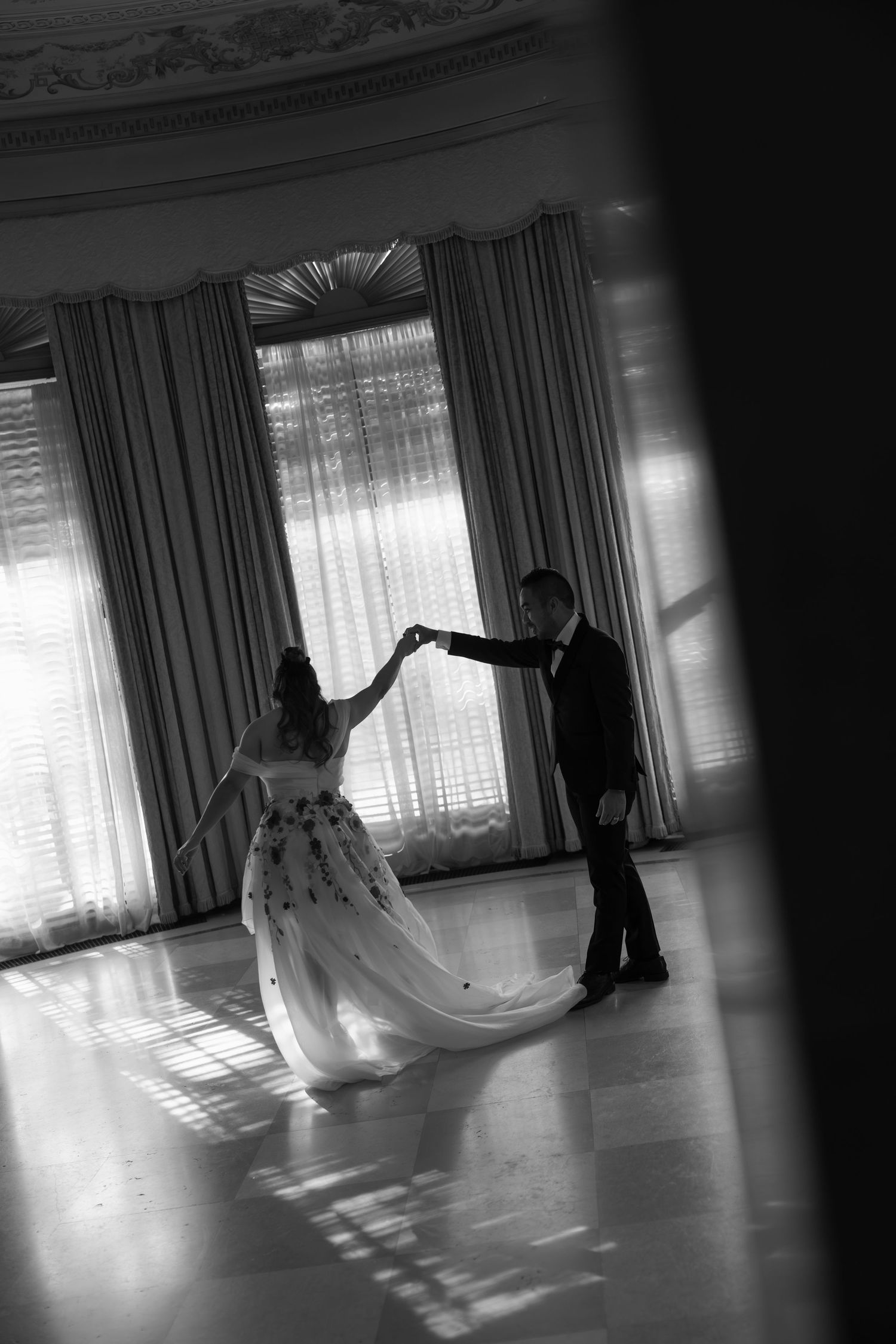 Black and white photo of bride and groom sharing first dance in elegant ballroom.