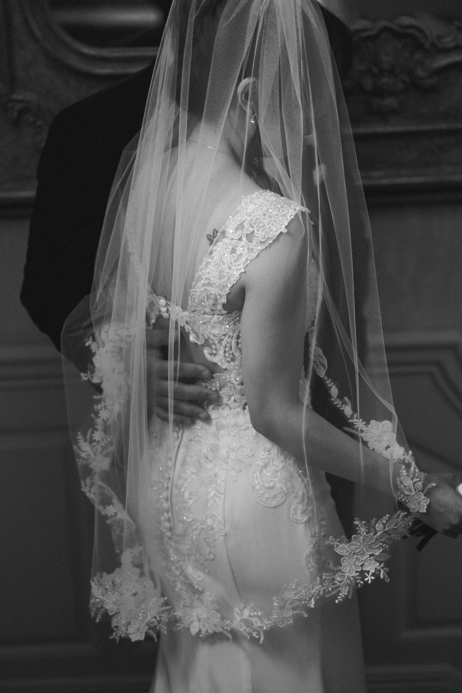 A black and white close-up of an elegant bridal gown with delicate lace veil and intricate back detailing.