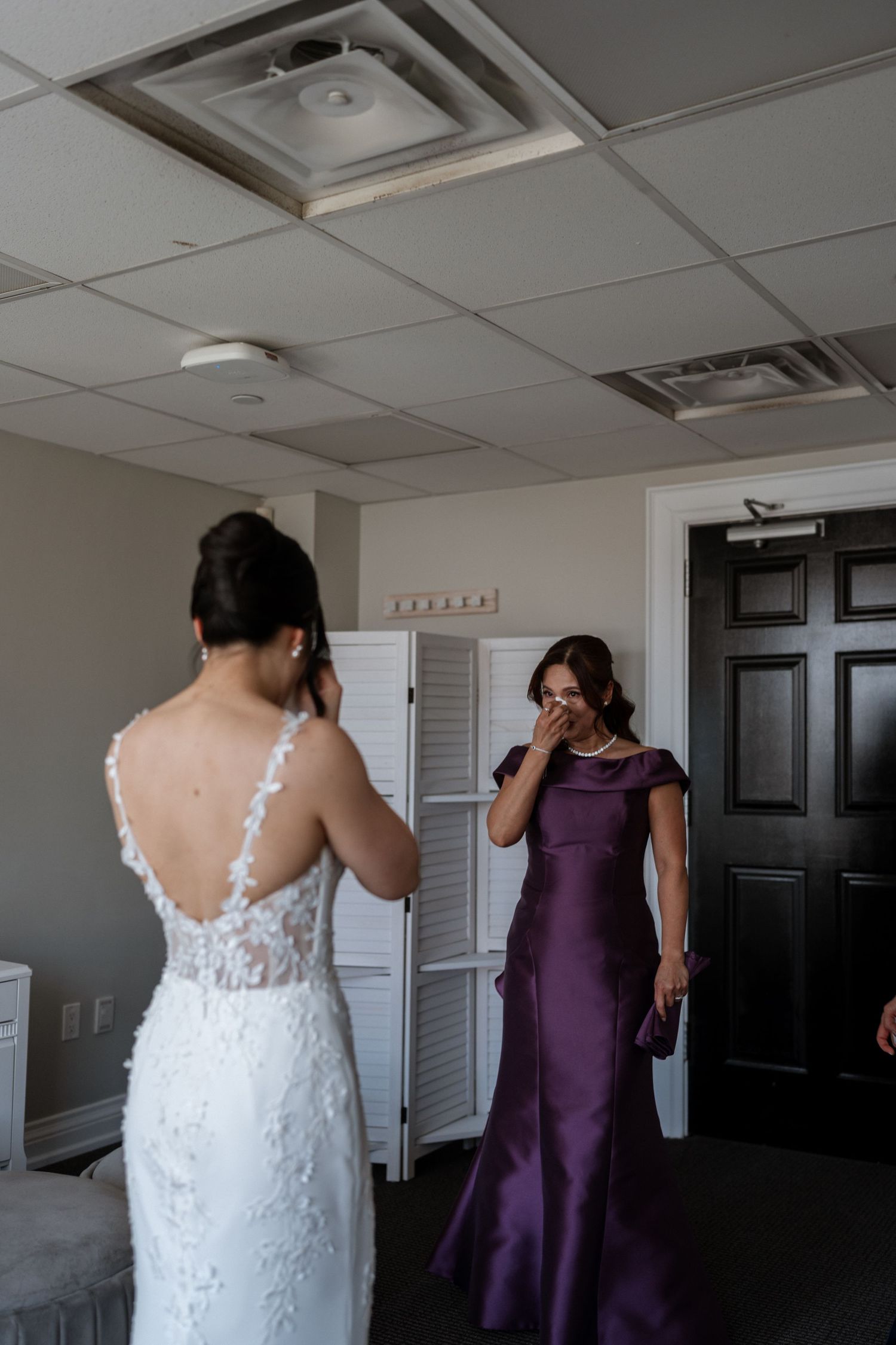An emotional first look moment between a bride in lace gown and a woman wearing an elegant purple evening dress.