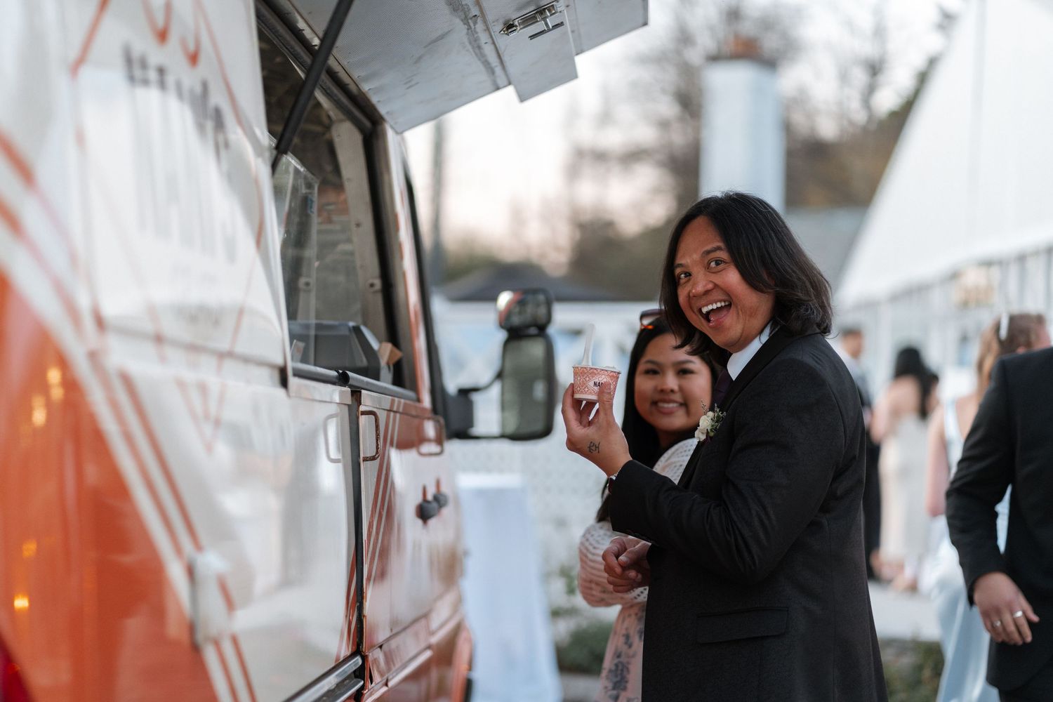 Two people laugh while ordering from a food truck at an outdoor event.