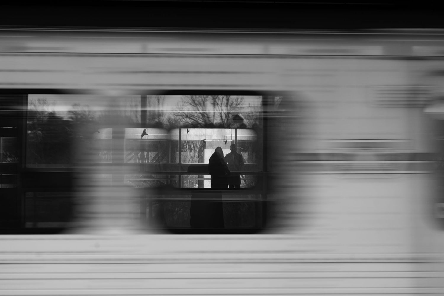 Black and white motion blur photo of two people waiting at a train or subway station platform.