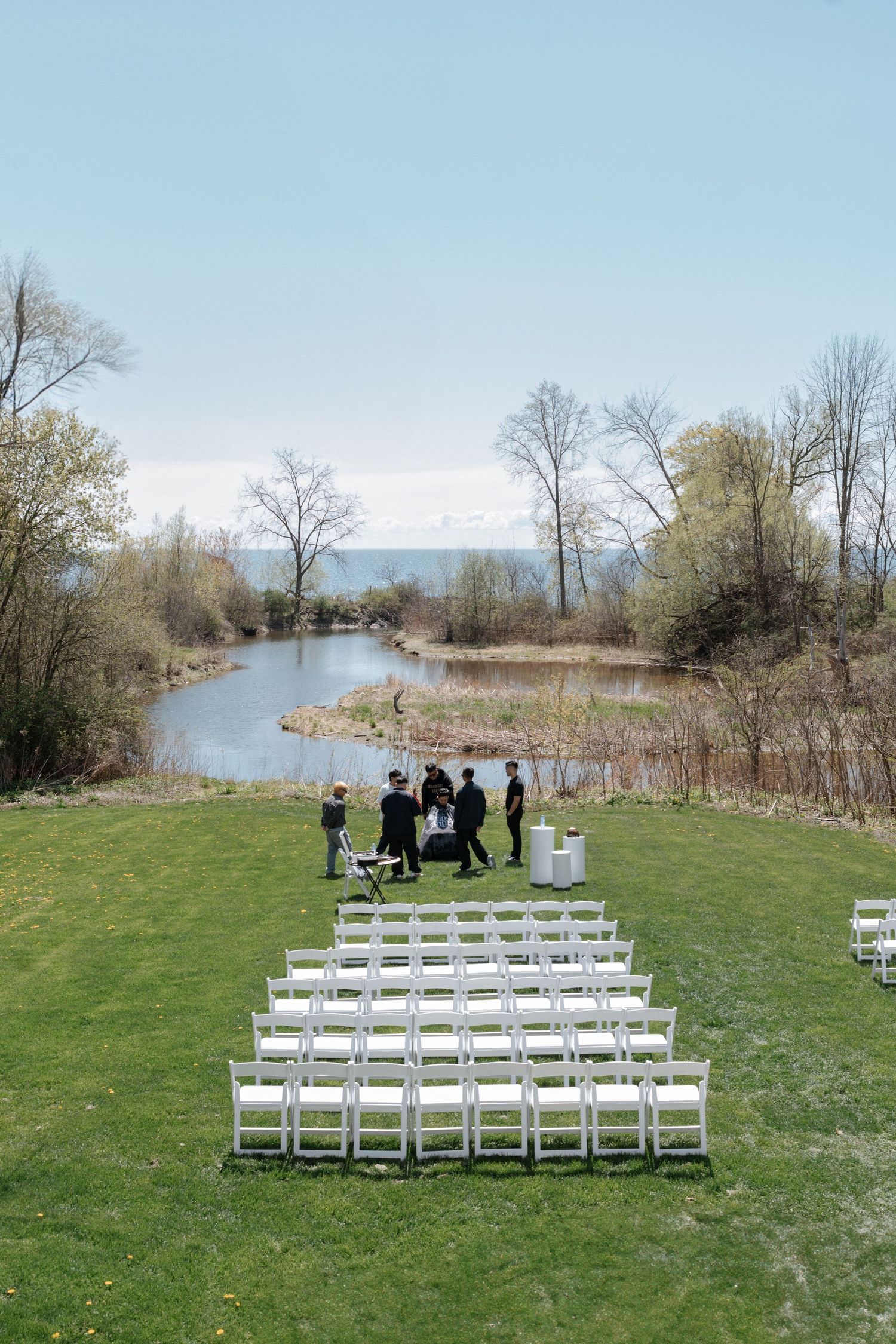 White folding chairs arranged for an outdoor wedding ceremony by a scenic river with trees and mountains in the background.