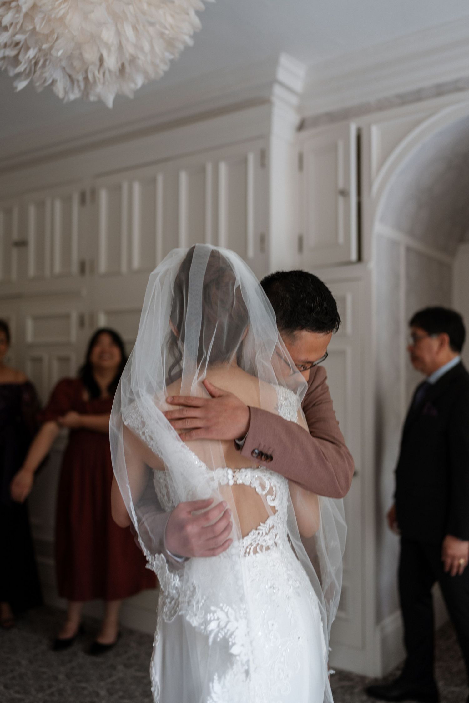 A tender embrace between newlyweds during their first dance at an elegant indoor wedding venue with white paneled walls.
