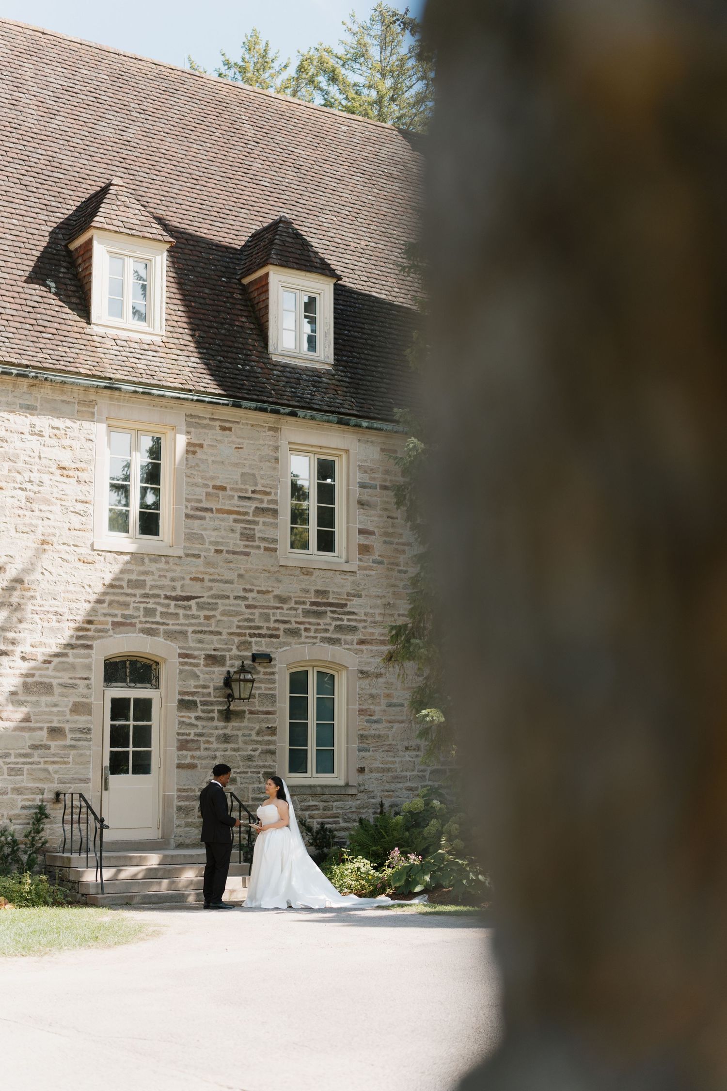 Bride and groom standing before a charming stone mansion on their wedding day.