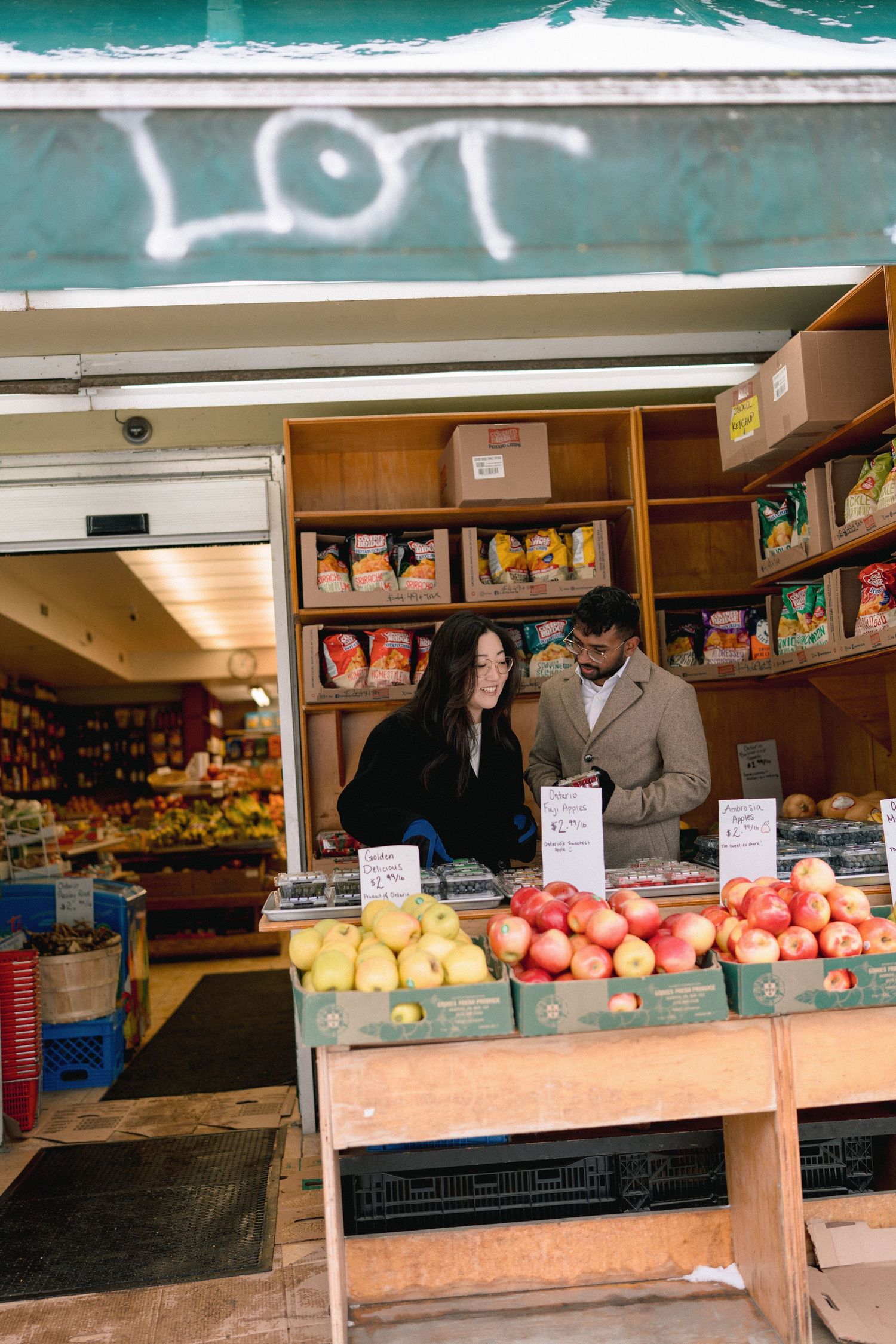 Couple shopping at an outdoor fruit market stand with fresh apples and produce on display.