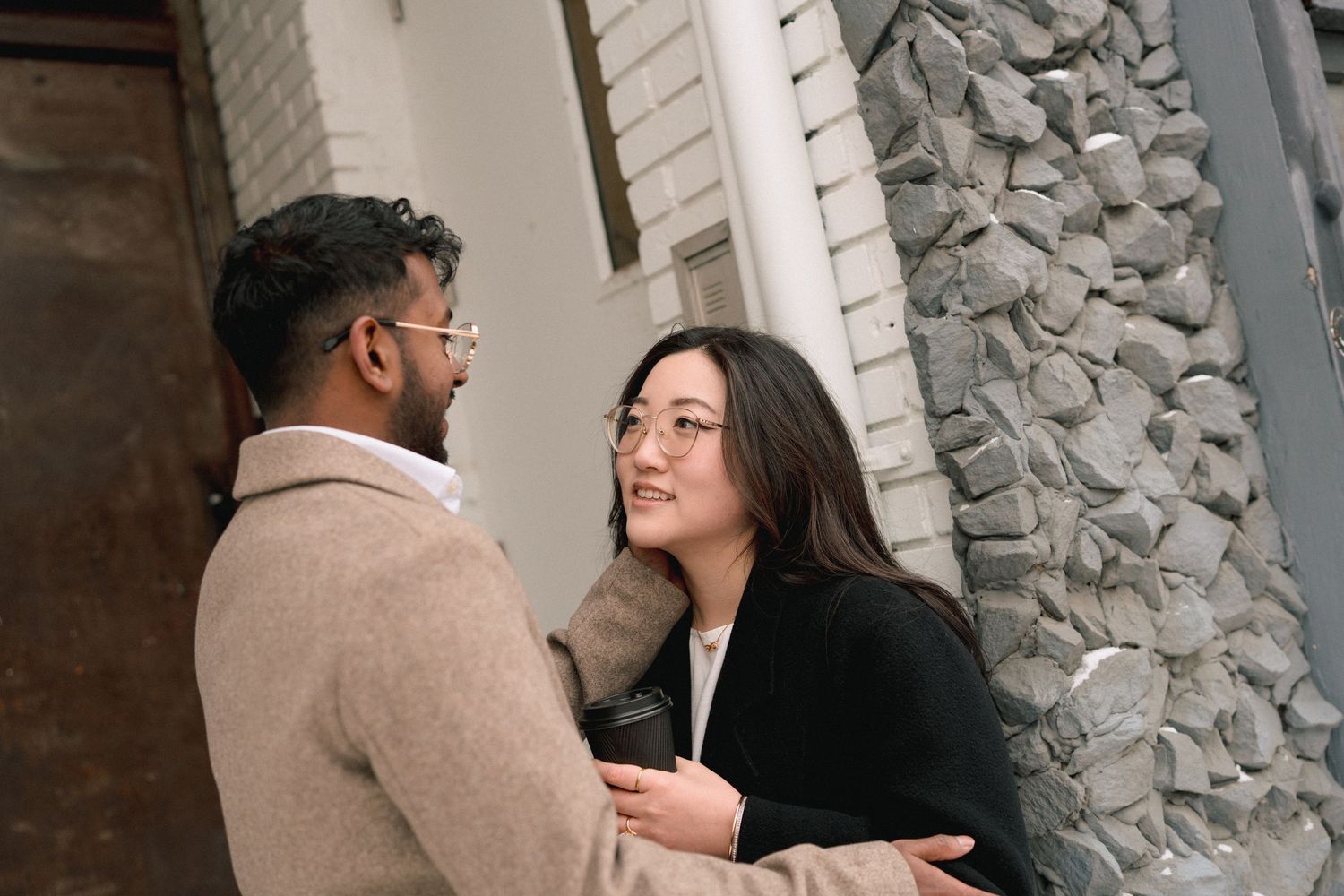A couple in formal attire shares an intimate moment against a textured stone wall background.