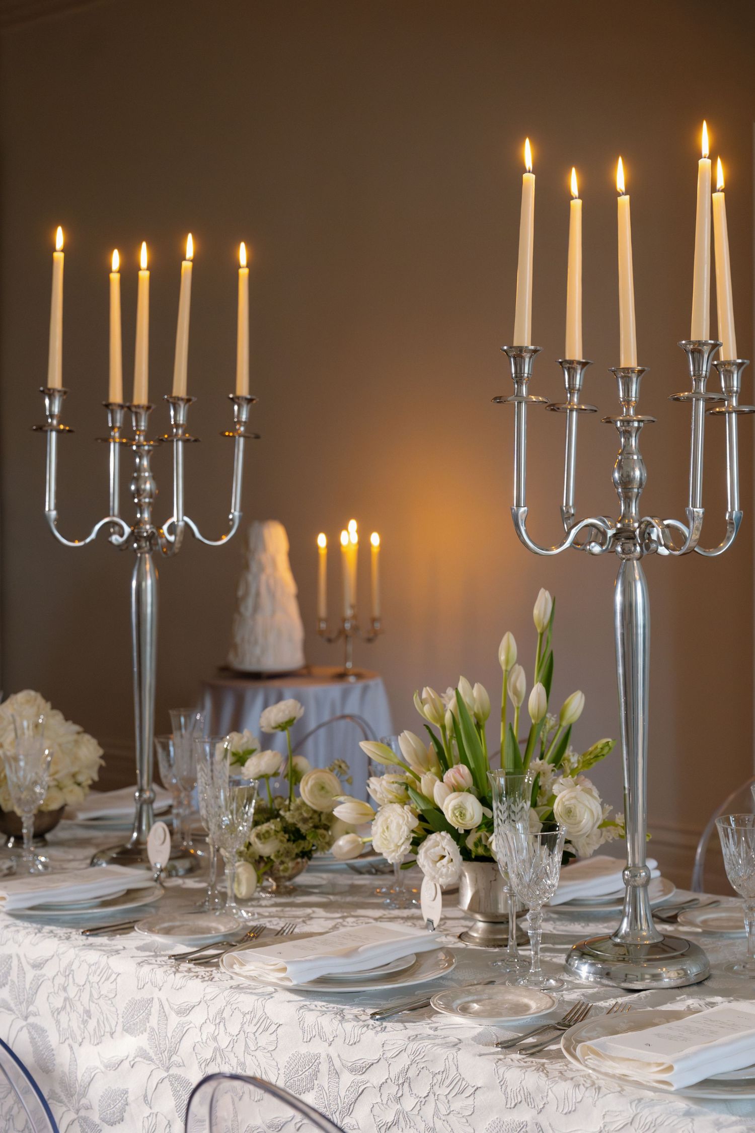 Silver candelabras with white candles flanking white floral centerpiece on a lace wedding table.