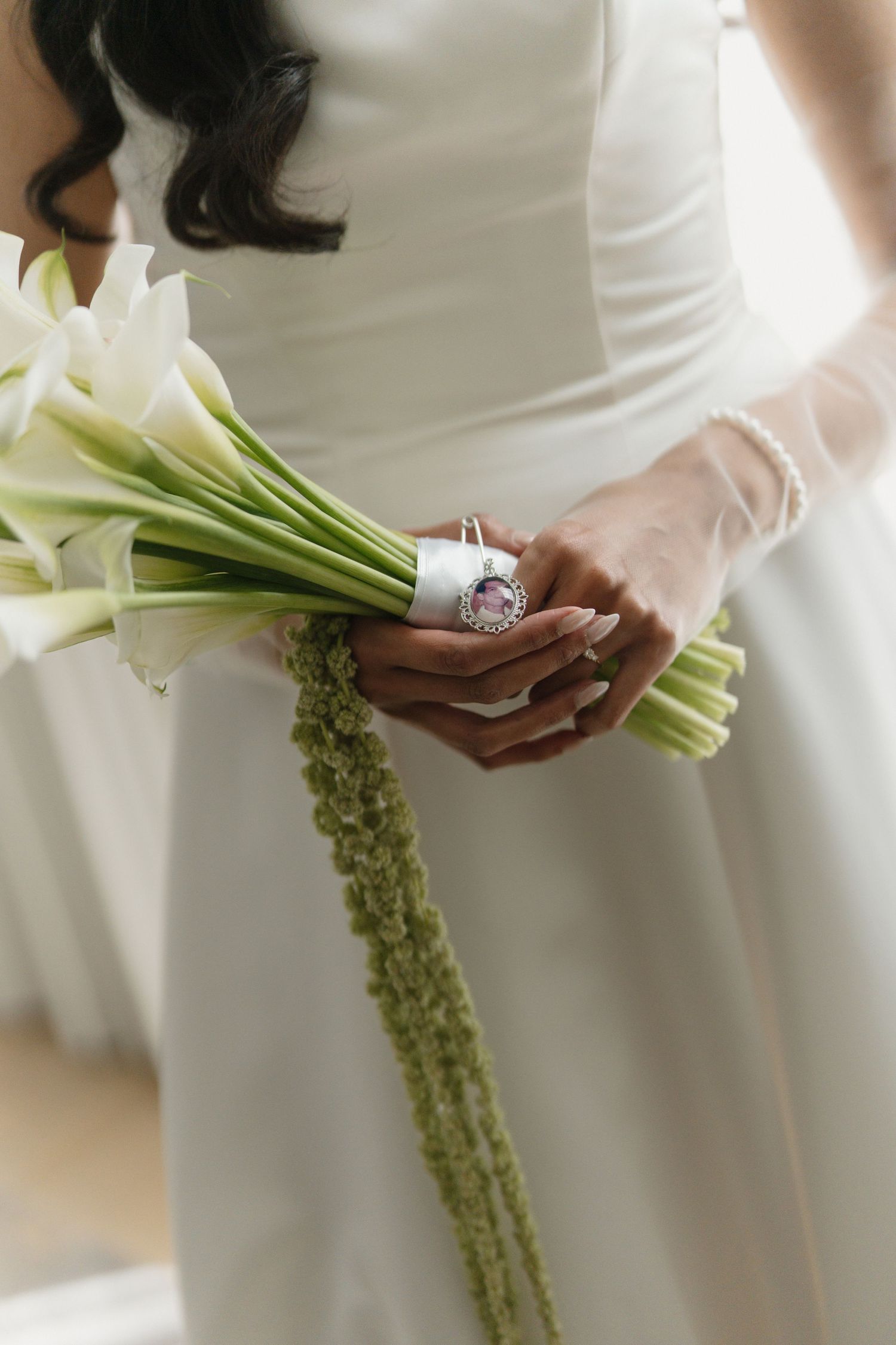 Bride in white gown holding elegant calla lily bouquet with green amaranthus, adorned with a silver and amethyst ring.