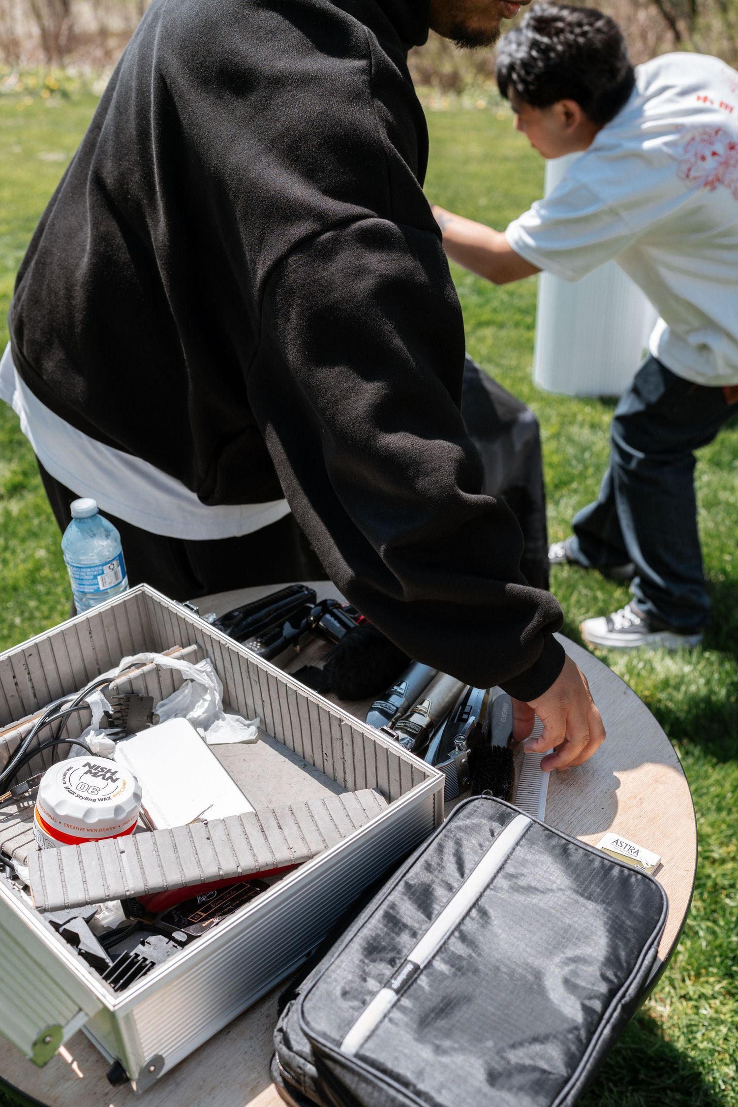 Camera equipment case with film supplies laid out on a table outdoors in grass with someone wearing black jacket.