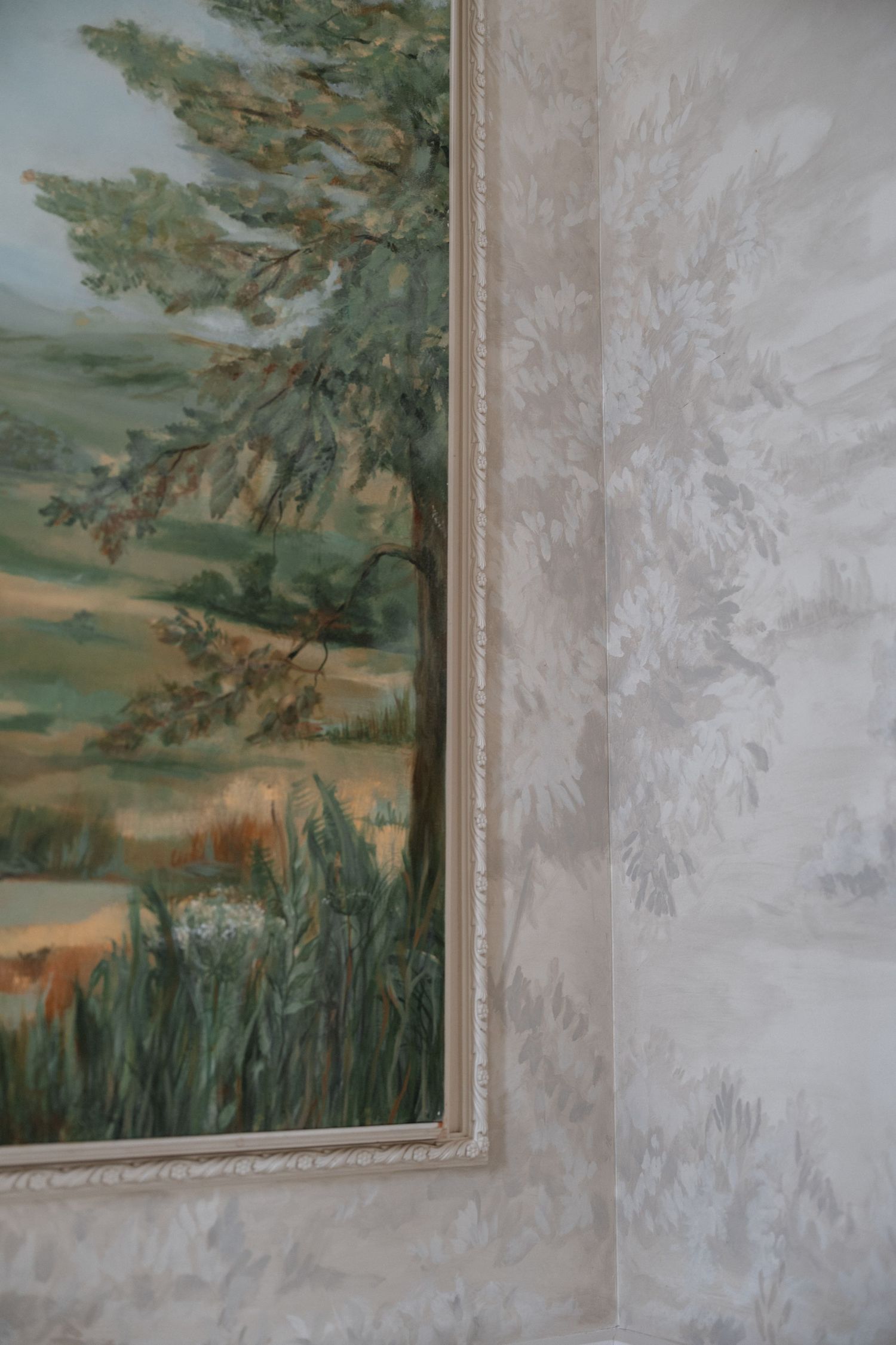 Close-up view of a painted mural showing green trees against a muted wall with textured finish.