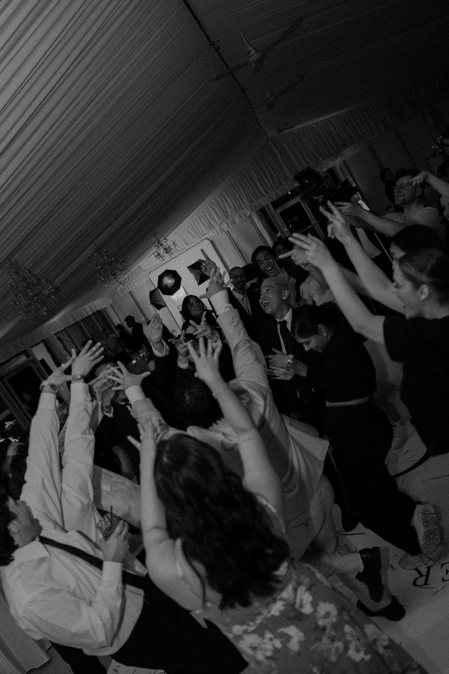 Black and white photo of crowd with raised hands at a lively concert or dance party in a packed indoor venue.