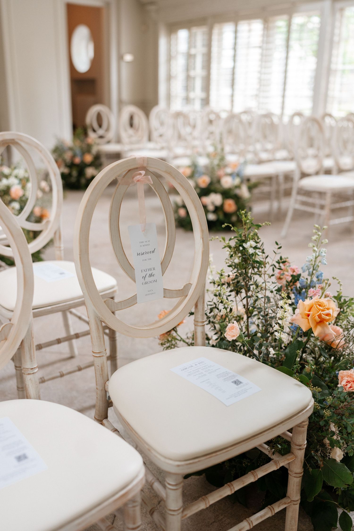 Elegant white chairs with circular backs arranged for a wedding ceremony with peach and blush floral arrangements.