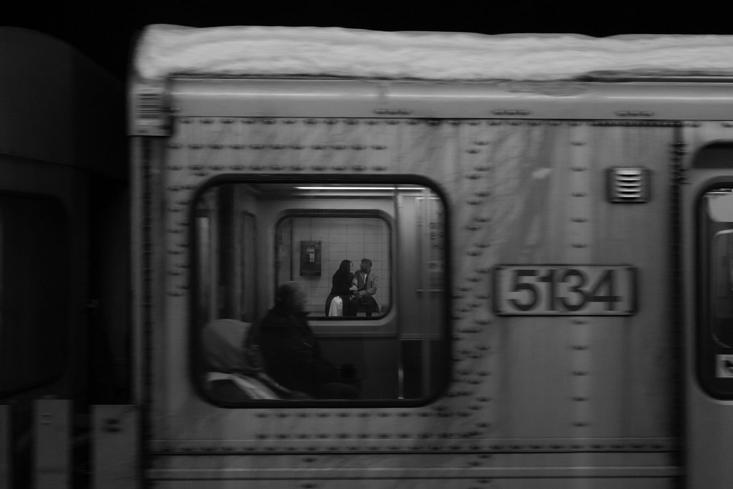 Black and white photograph of commuters looking out subway car windows during their daily journey in New York City.