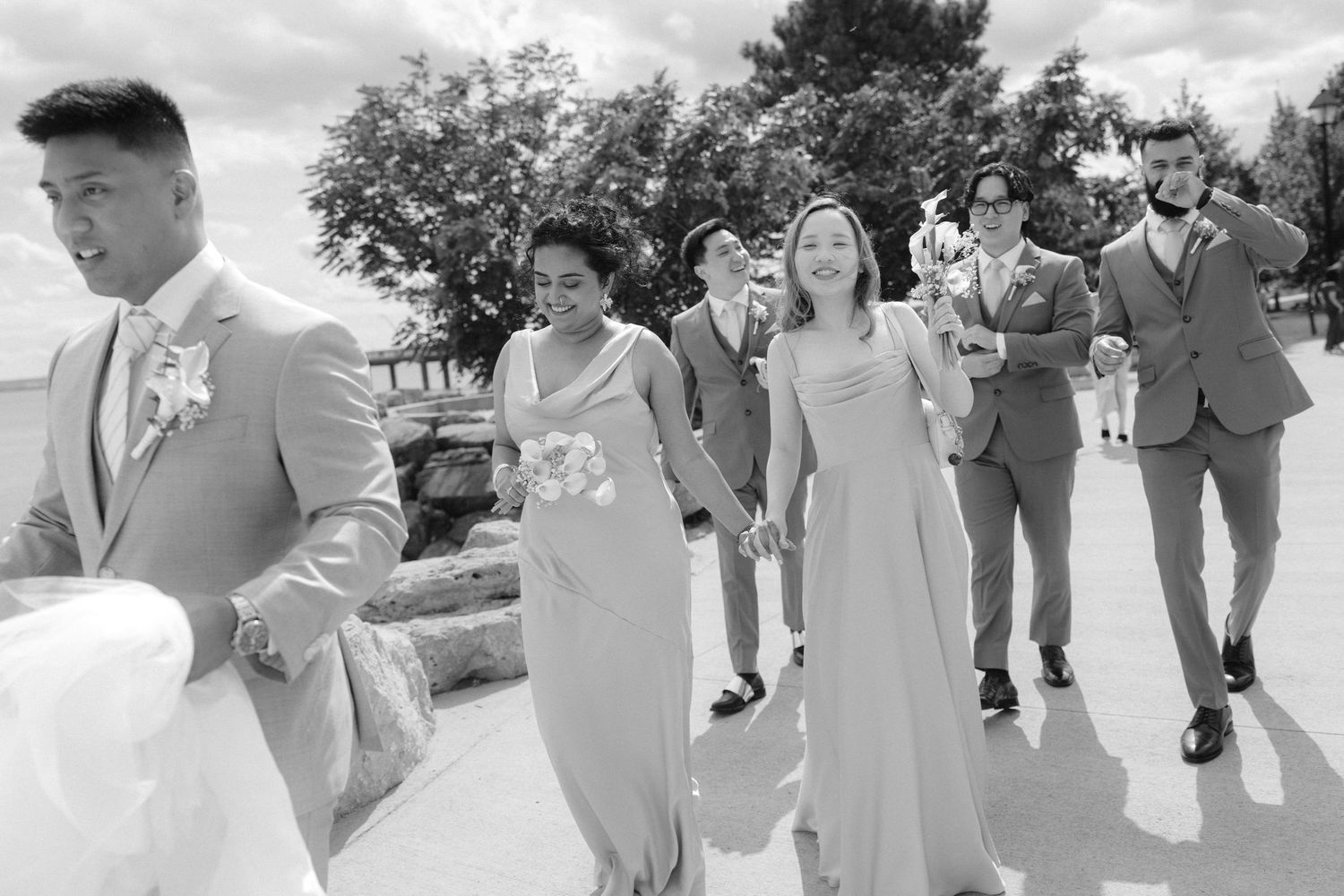 Black and white photo of wedding party walking together outdoors, bridesmaids in long gowns and groomsmen in suits.