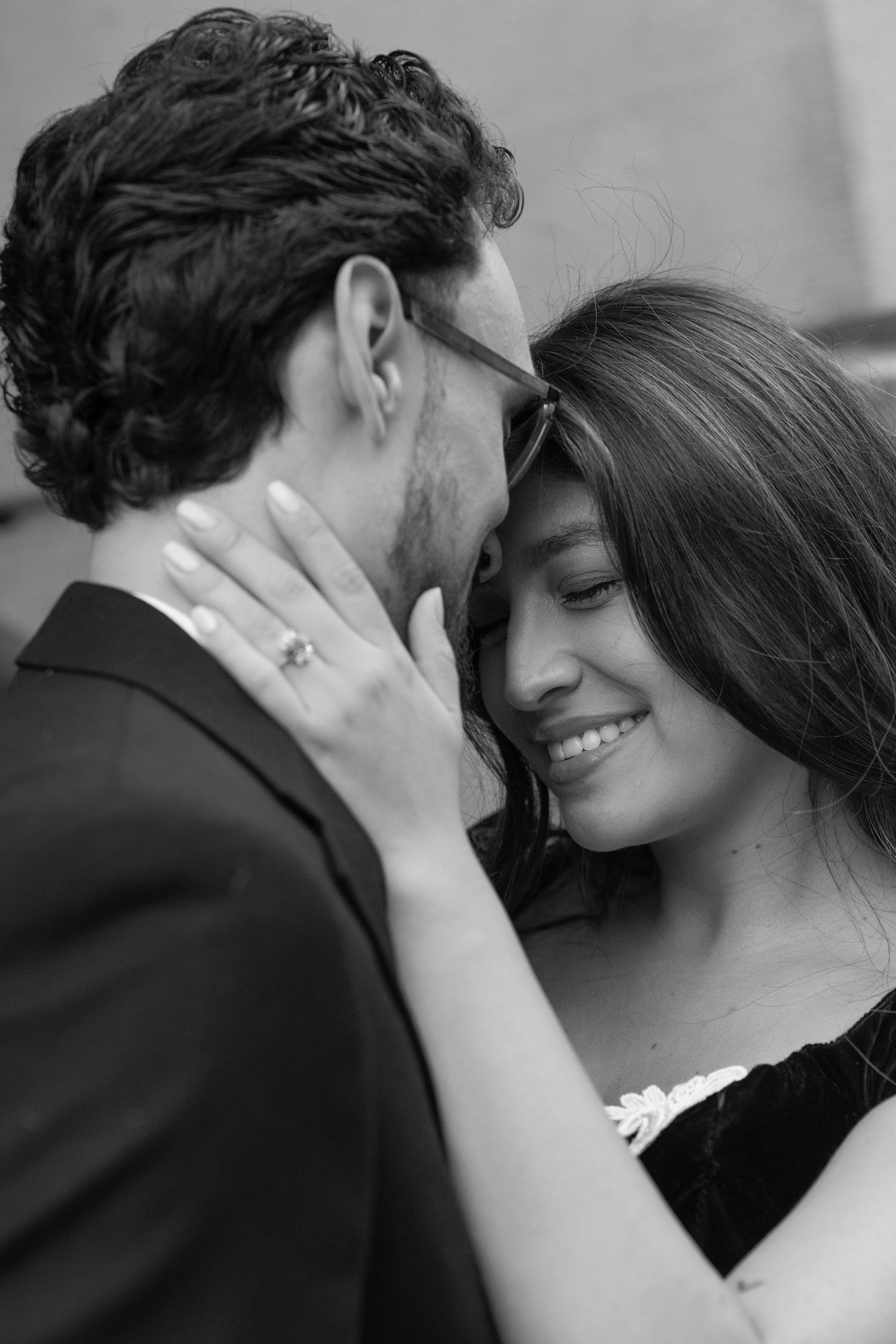 Black and white close-up of a couple sharing an intimate moment, woman smiling with engagement ring visible.