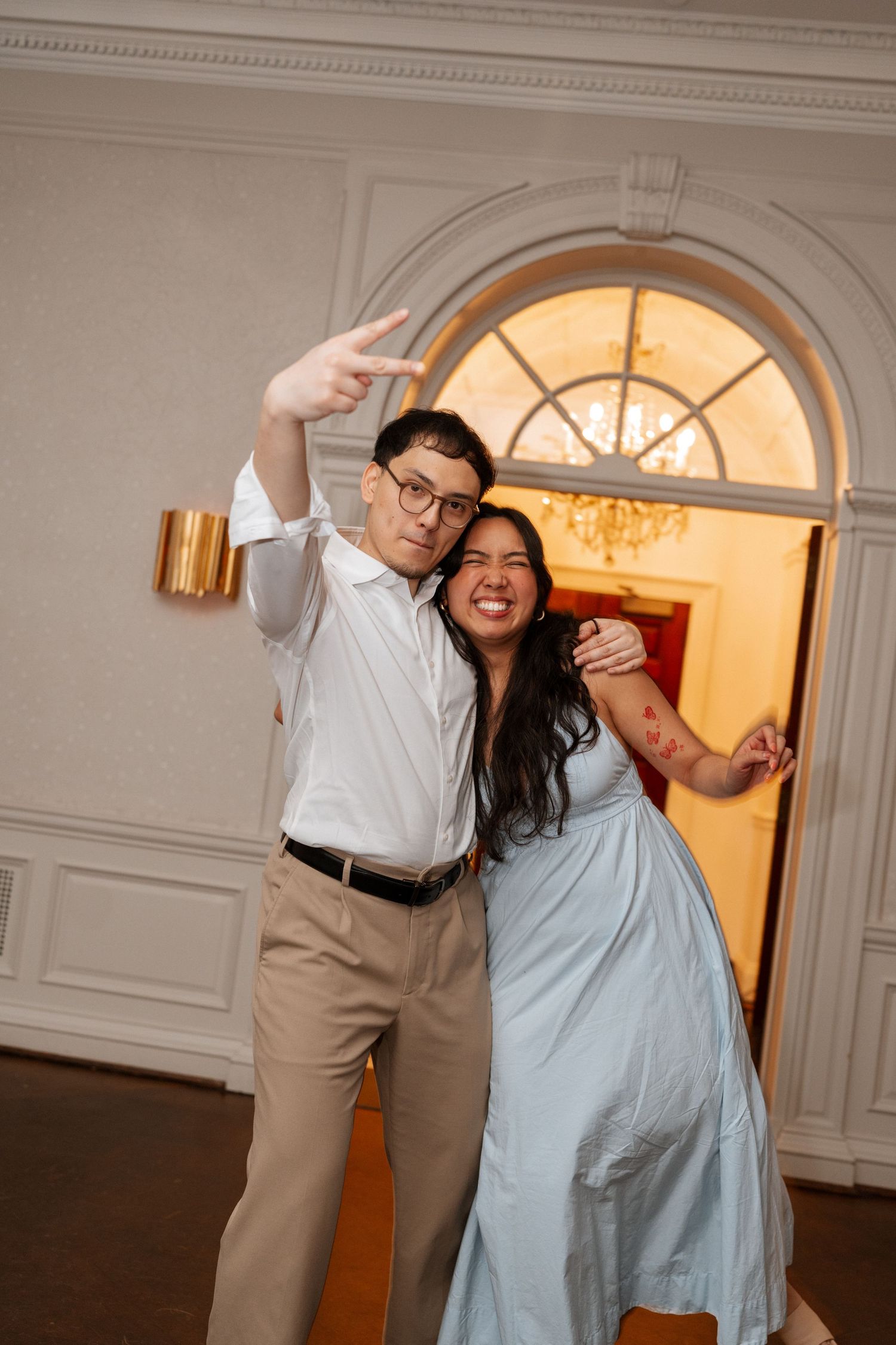 A couple in formal attire dances and laughs together under an elegant arched doorway with crown molding.