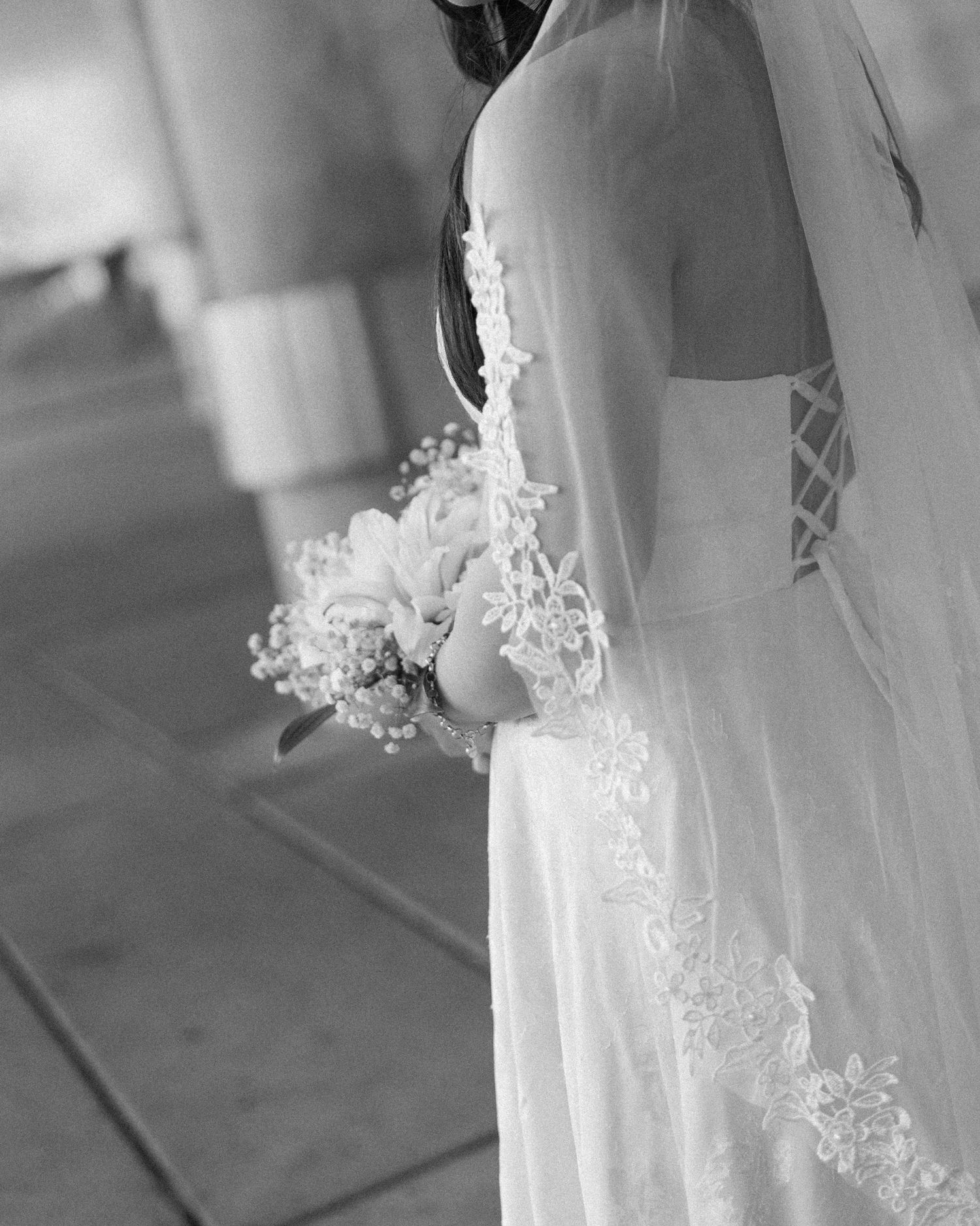 Black and white photo of a bride in a lace-trimmed veil holding a floral bouquet, showcasing an elegant corset wedding dress.